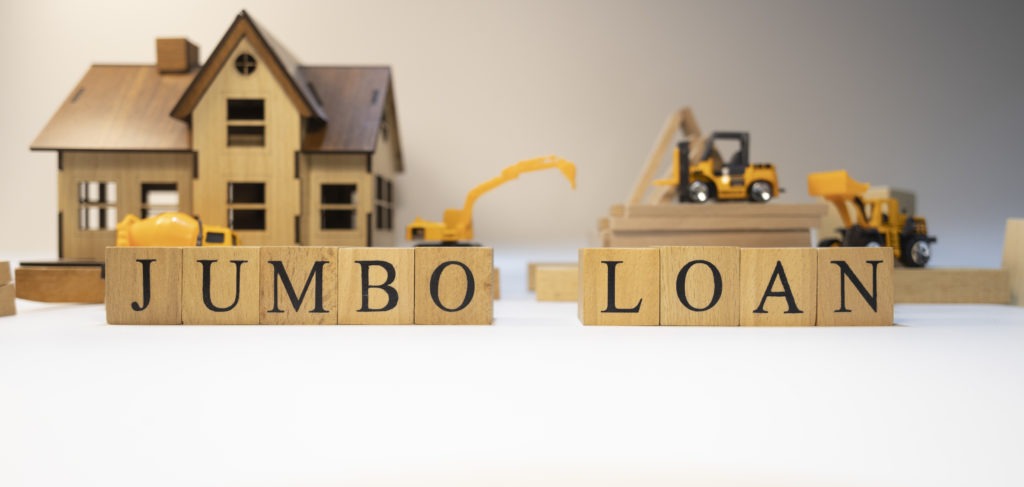 A small wooden house surrounded by miniature construction vehicles with the words “Jumbo Loan” displayed, representing financing for large properties.