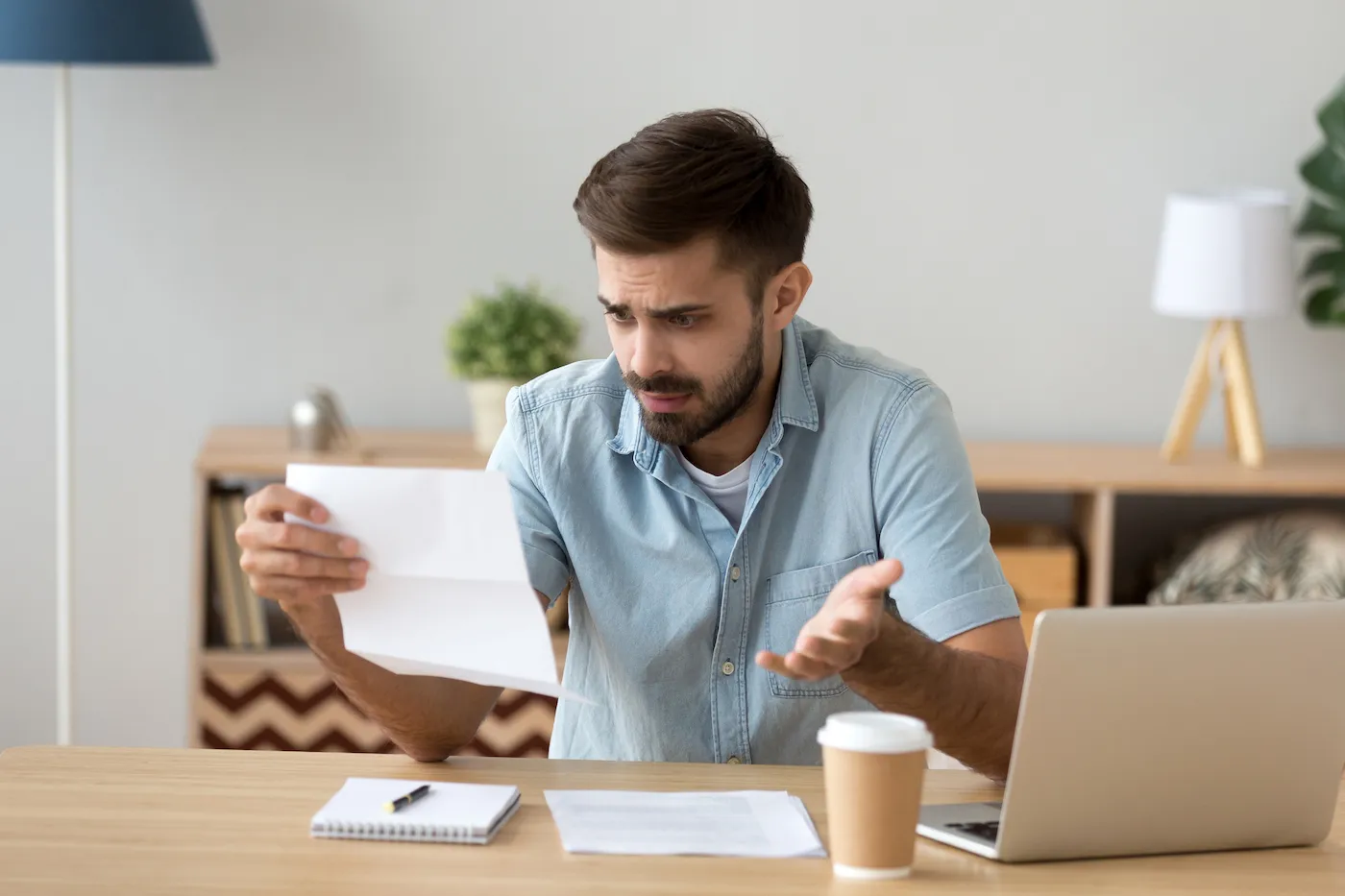 A man looking confused while reading a document notifying him that his personal loan application was rejected.