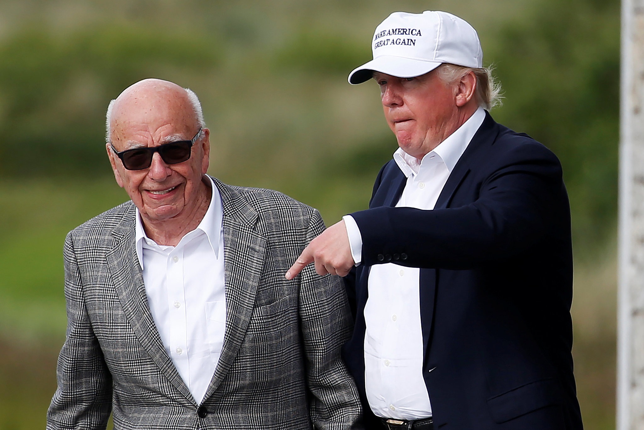 Donald Trump and Rupert Murdoch walking together on a golf course, appearing deep in conversation about business.