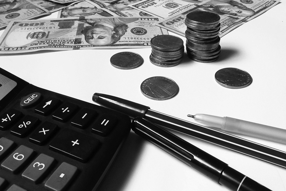 A calculator, pen, and cash arranged on a wooden table, symbolizing financial planning and budgeting.