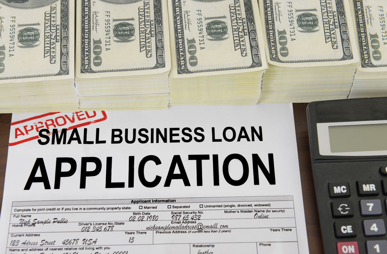 Small business loan documents on a desk with a calculator and stacks of cash, representing financial planning and loan calculation.