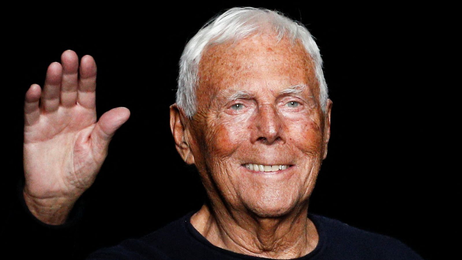 Giorgio Armani waving to the crowd at a recent public appearance, dressed casually.