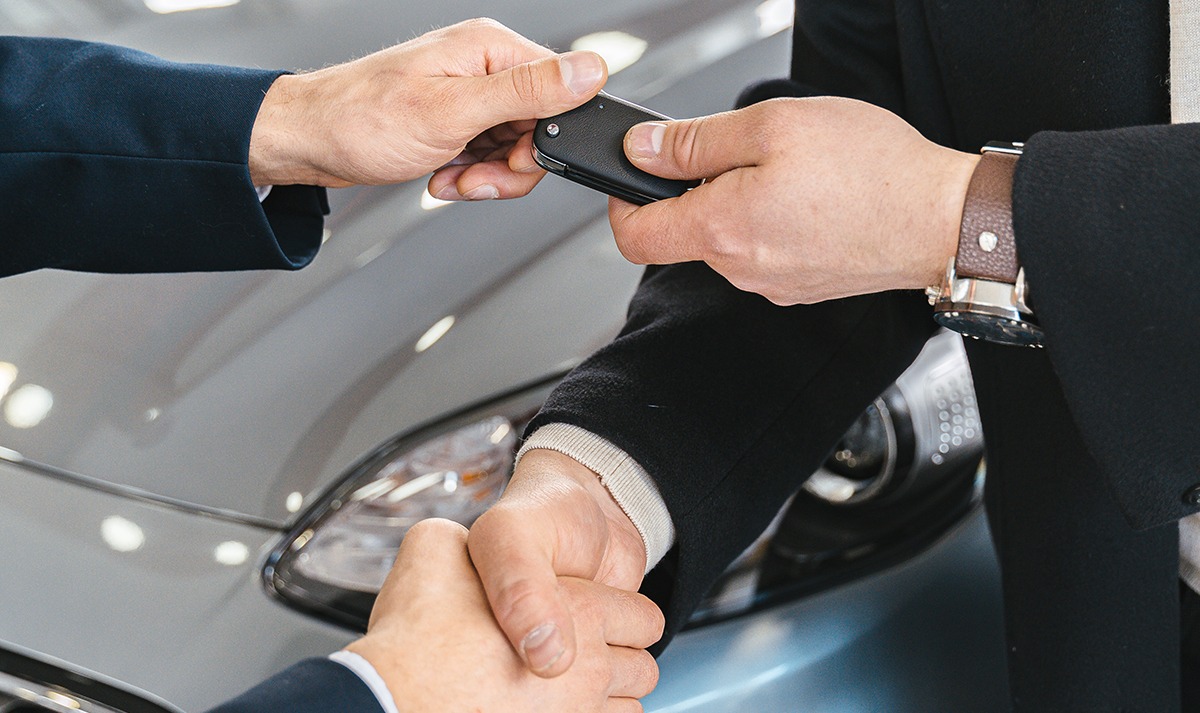 Car salesman handing over the keys of a new vehicle to a business owner, symbolizing a completed business car purchase.