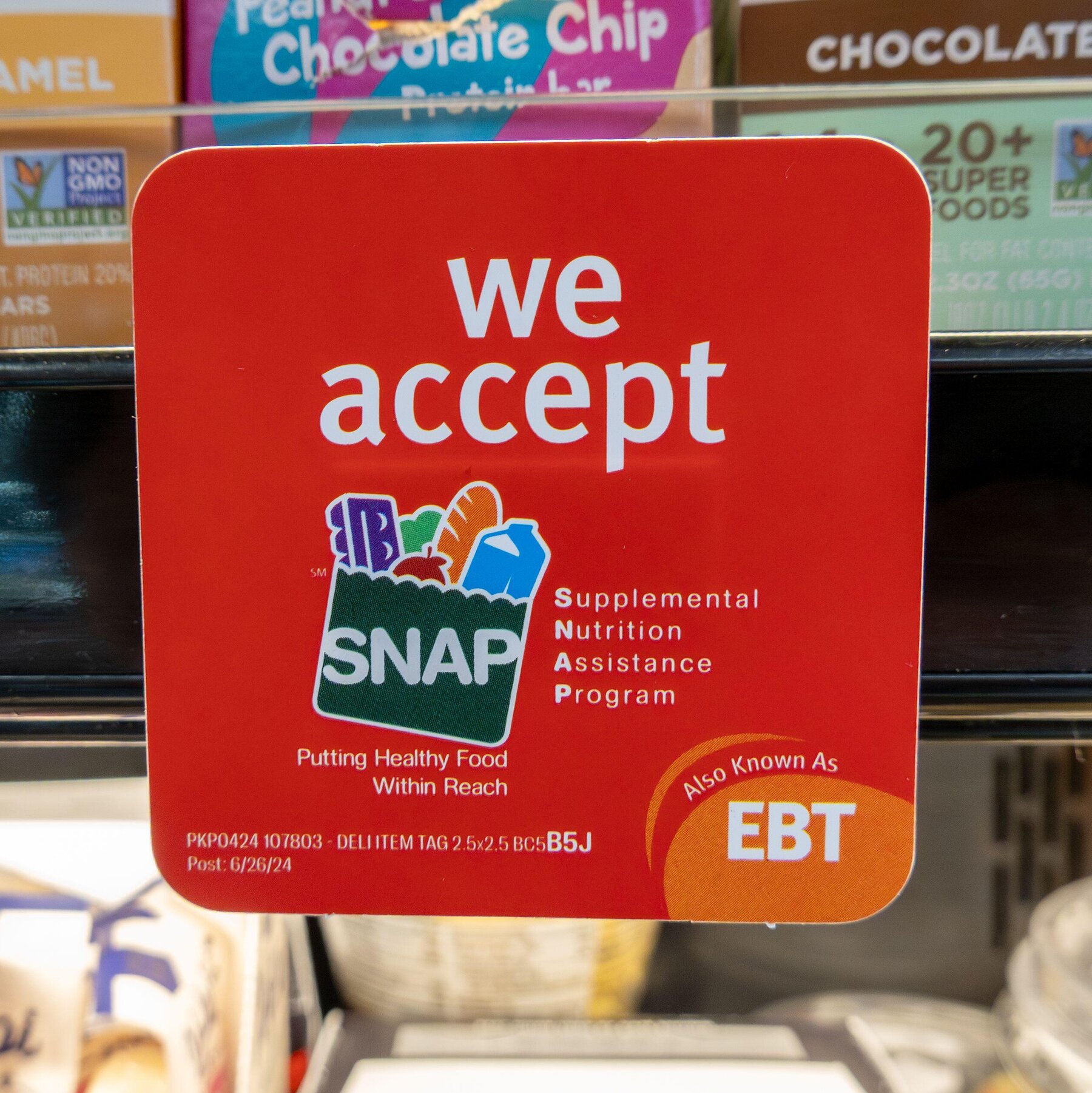 A red sign inside a grocery store that reads “We accept SNAP – Supplemental Nutrition Assistance Program,” indicating that EBT food stamp payments are accepted for eligible groceries.