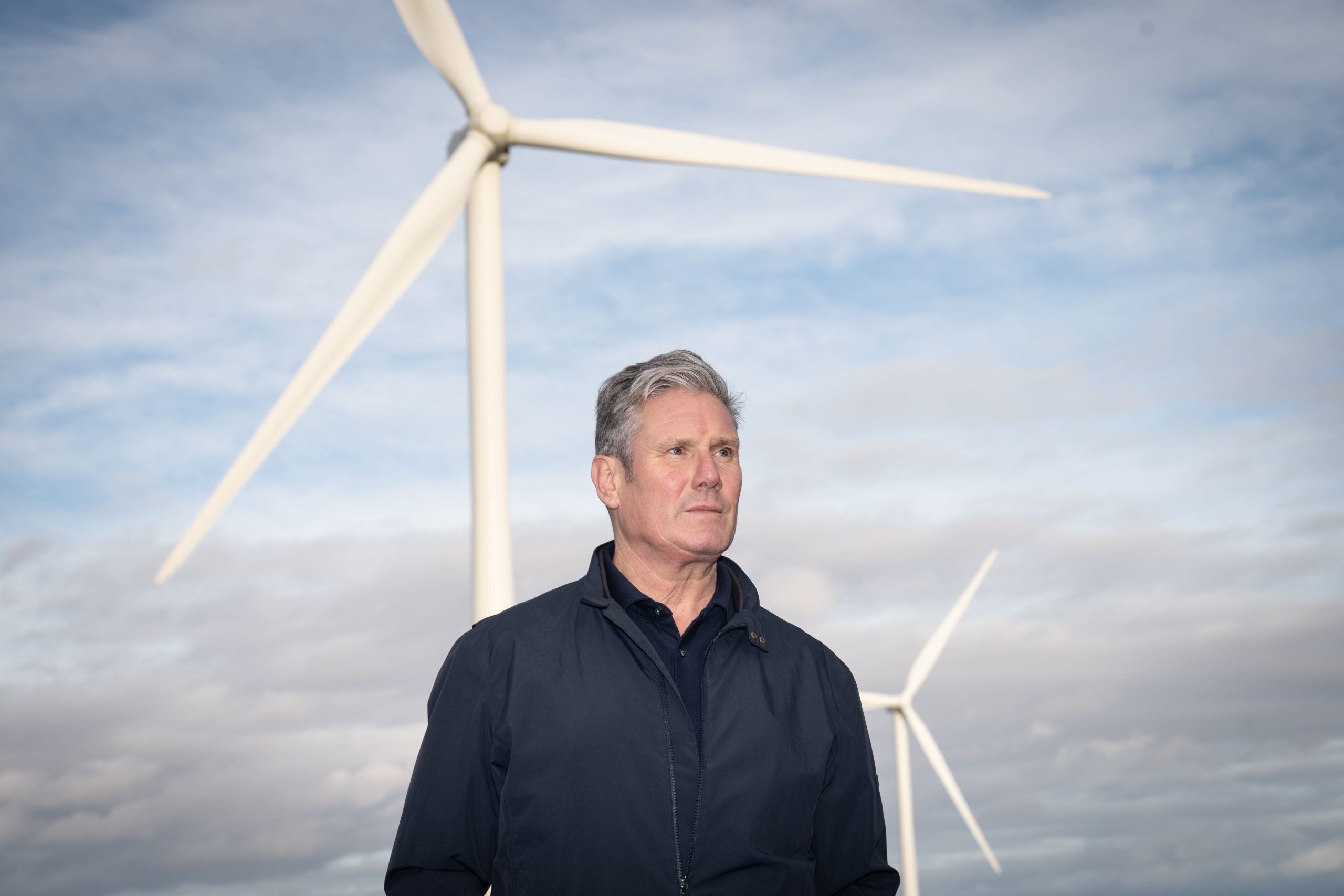 UK Prime Minister Keir Starmer standing in front of large offshore wind turbines during a visit to a renewable energy site, highlighting the government’s clean energy strategy.