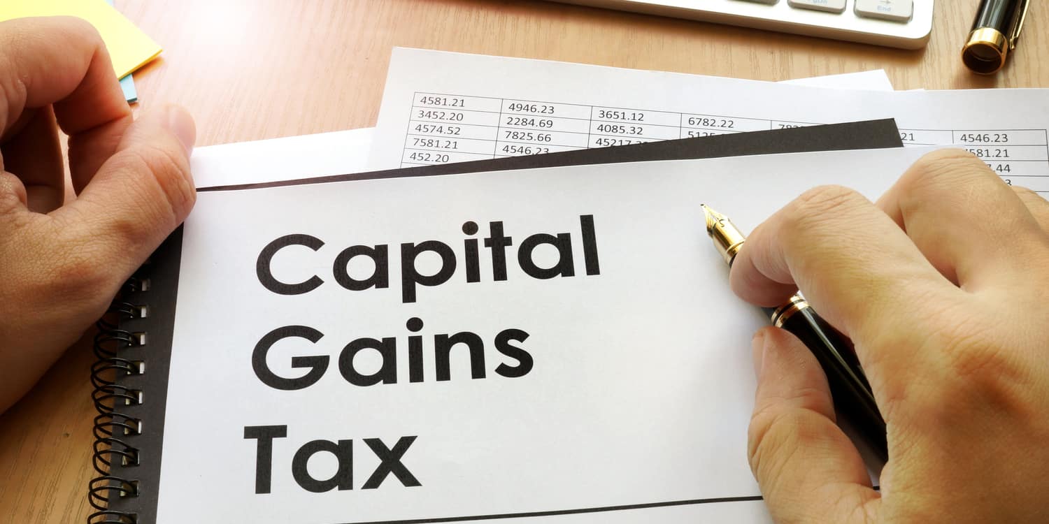A businessman holding a folder labeled “Capital Gains Tax,” representing financial planning and tax management for investments.