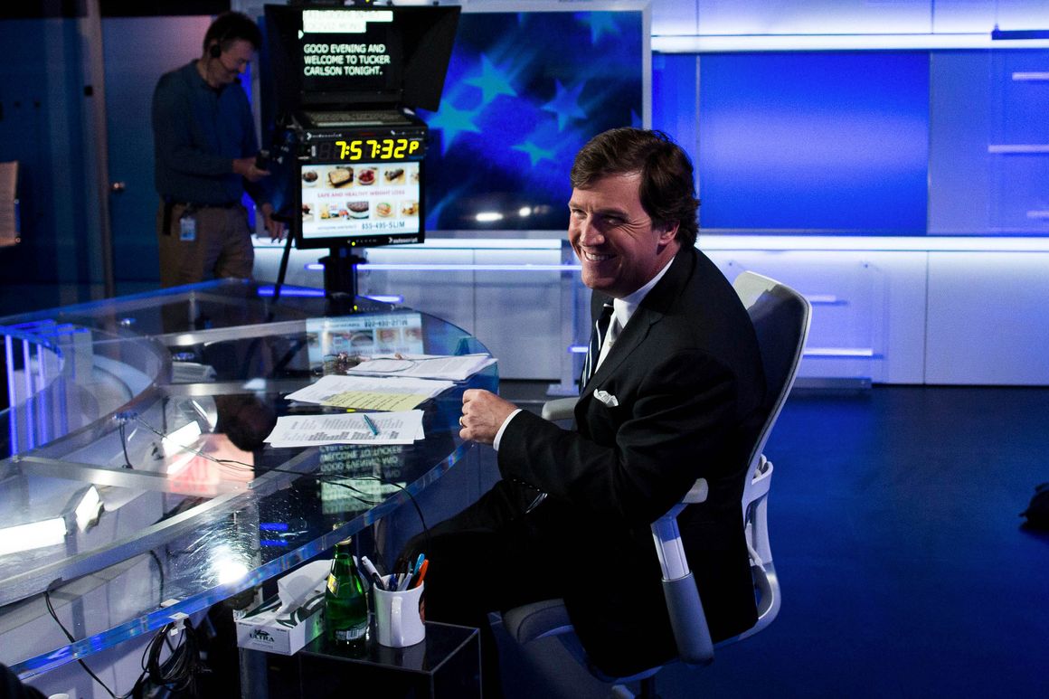 Tucker Carlson smiling behind the news desk in a behind-the-scenes moment.