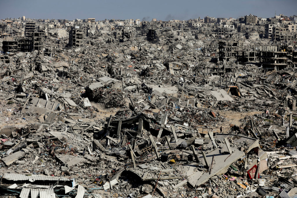 Aerial view of Gaza showing widespread rubble and destroyed buildings, streets filled with debris, and the scale of devastation across the city.