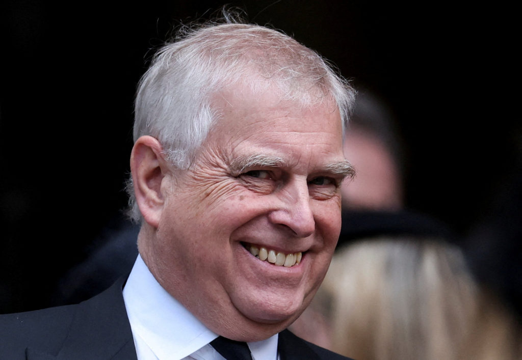Prince Andrew smiling while attending a recent royal funeral, dressed in formal attire.