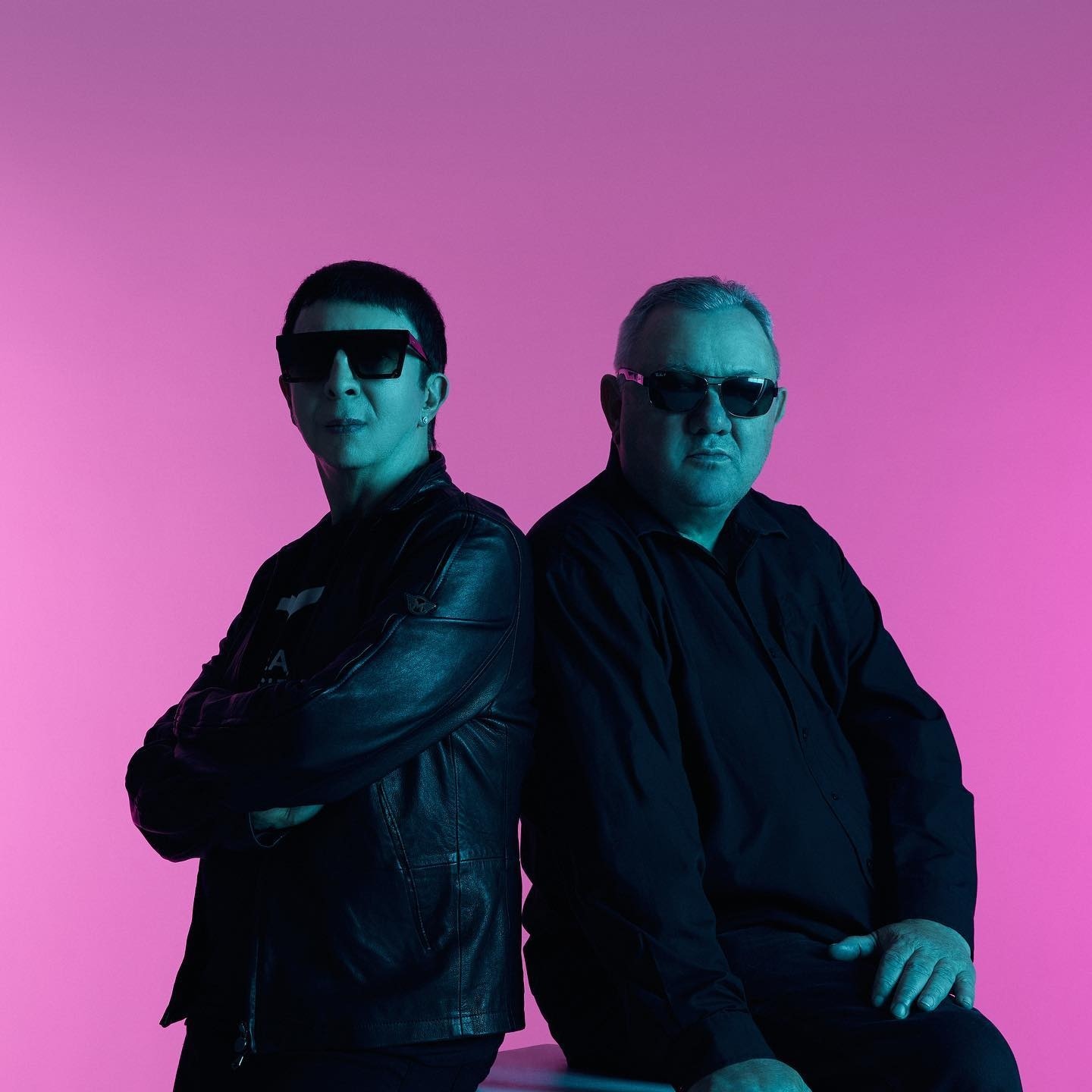 A striking promotional image of the synth-pop duo Soft Cell, featuring Marc Almond and David Ball, posed against a vibrant purple background.