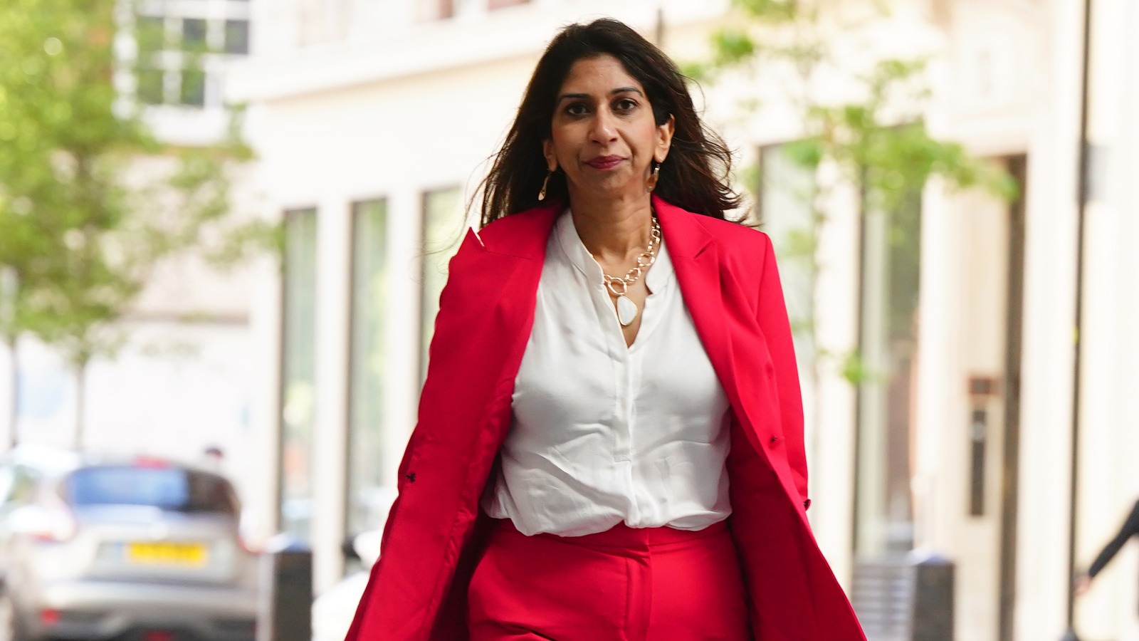 Suella Braverman walks confidently down Downing Street in a pink suit, reflecting her high-profile role as Home Secretary and prominent political figure.