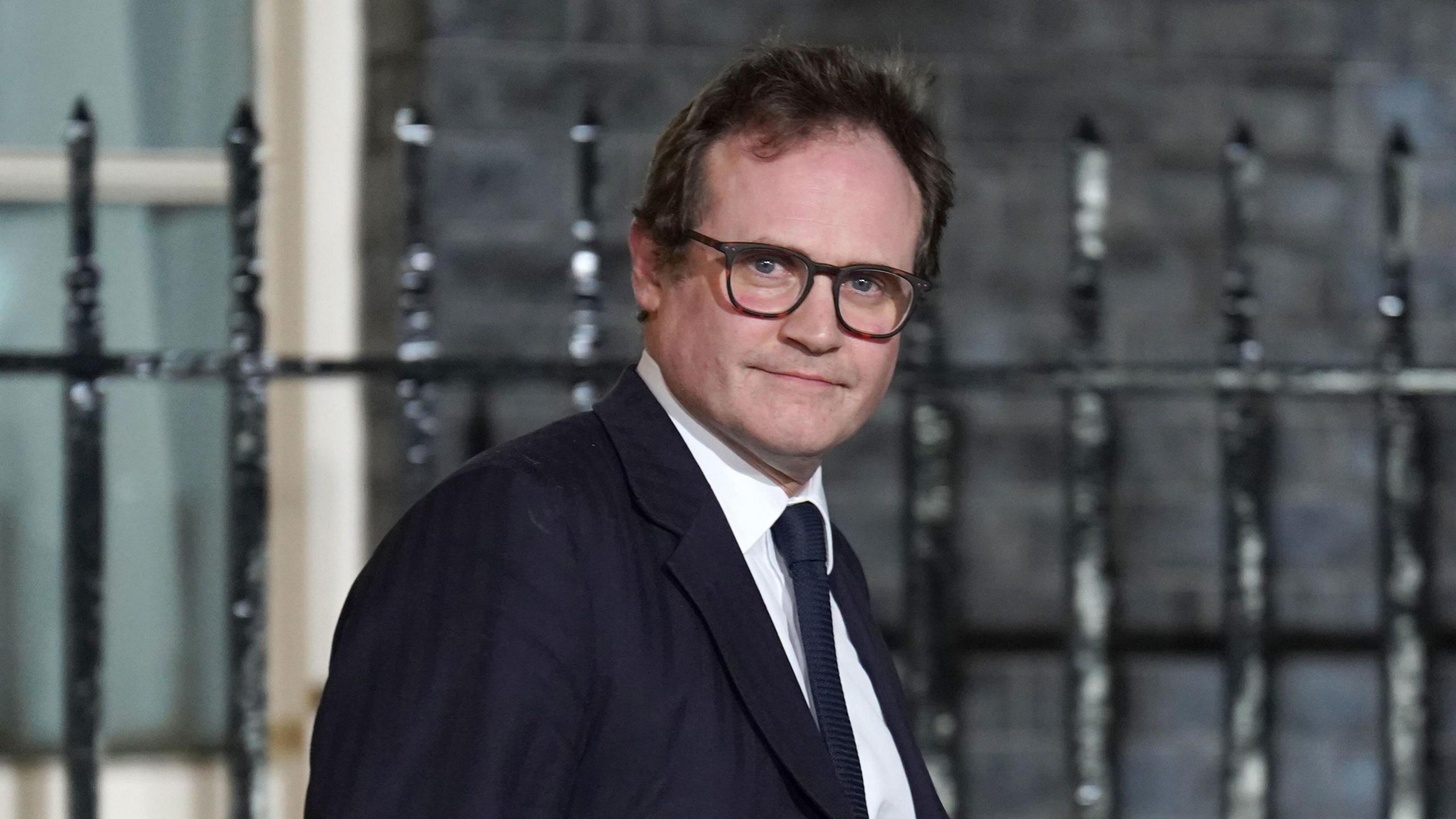 Tom Tugendhat walking down Downing Street, smiling confidently in a suit.