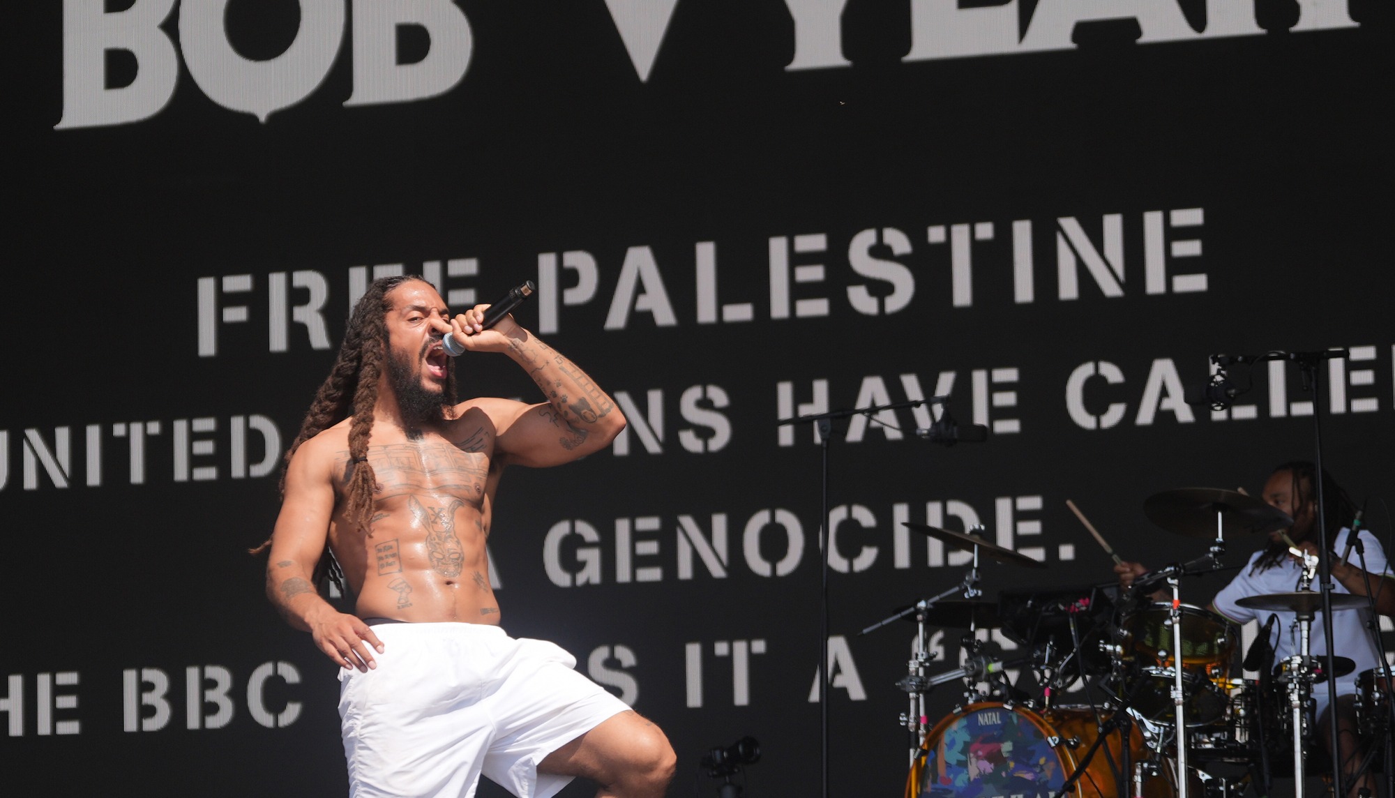 Bob Vylan performing on stage at Glastonbury Festival, with frontman Bobby Vylan leading the crowd in a controversial chant during their live set.