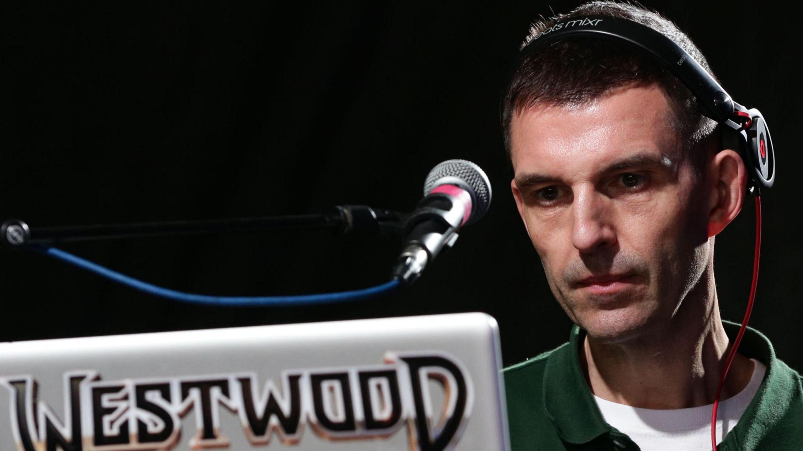 Tim Westwood hosting his radio show in the studio, seated behind a laptop and mixing console.