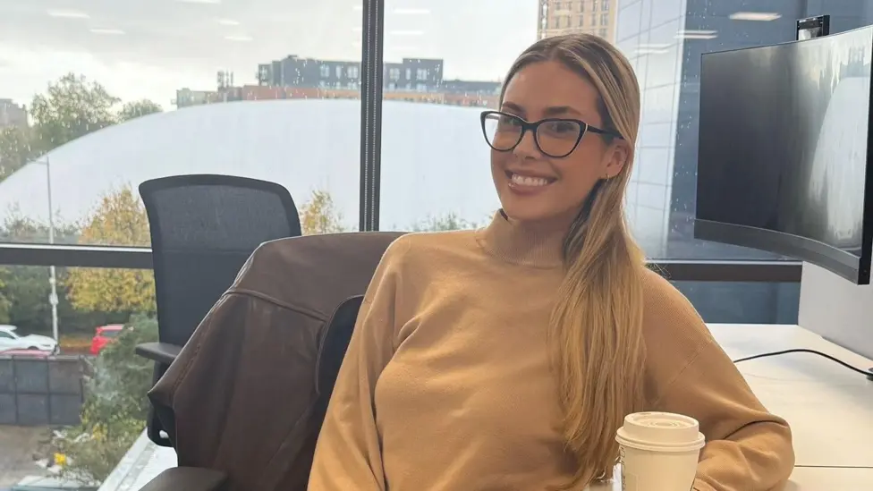Ellie Jackson at her desk in a corporate office, working on her laptop.
