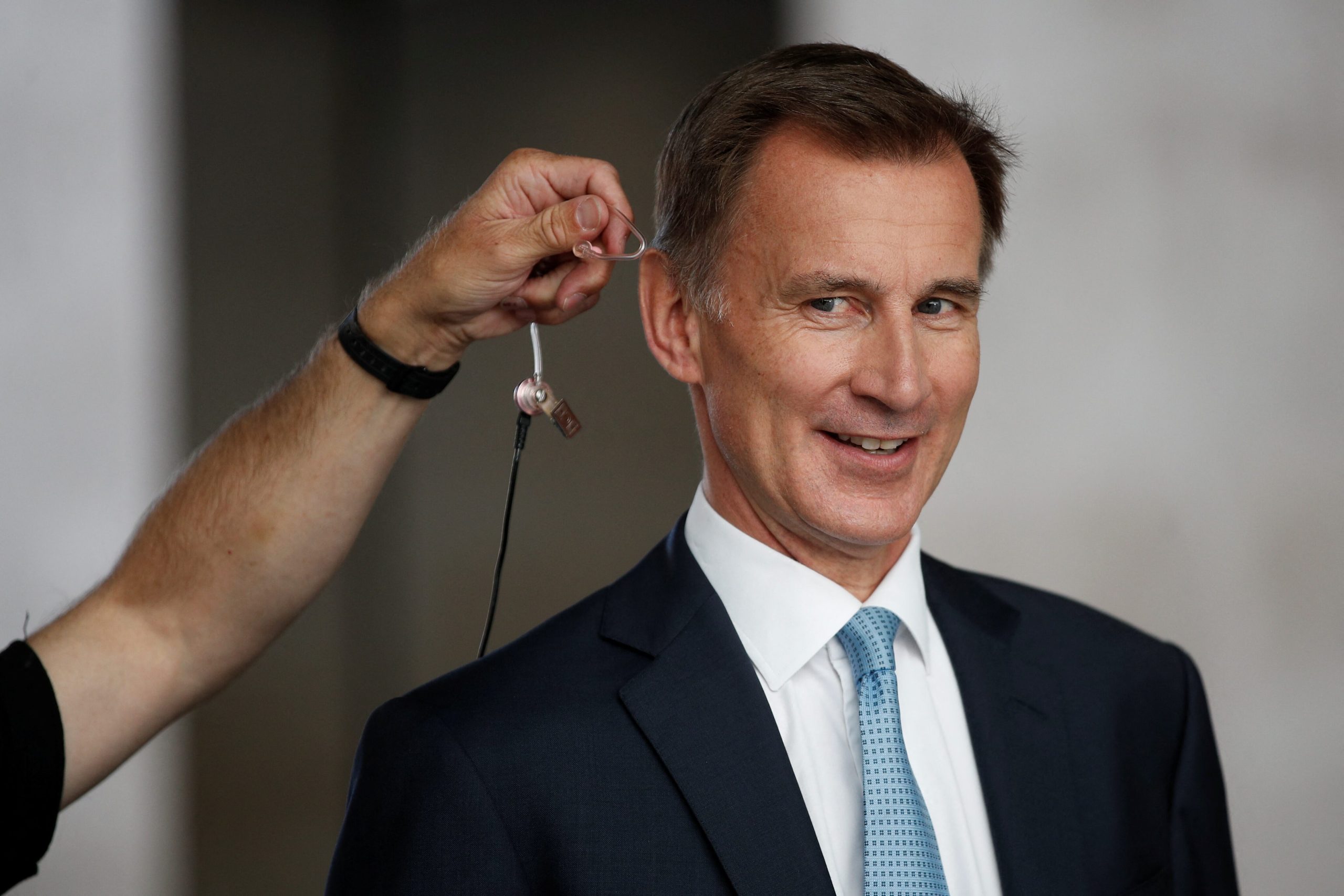 Jeremy Hunt smiling as he gets a microphone clipped on in preparation for a media interview.