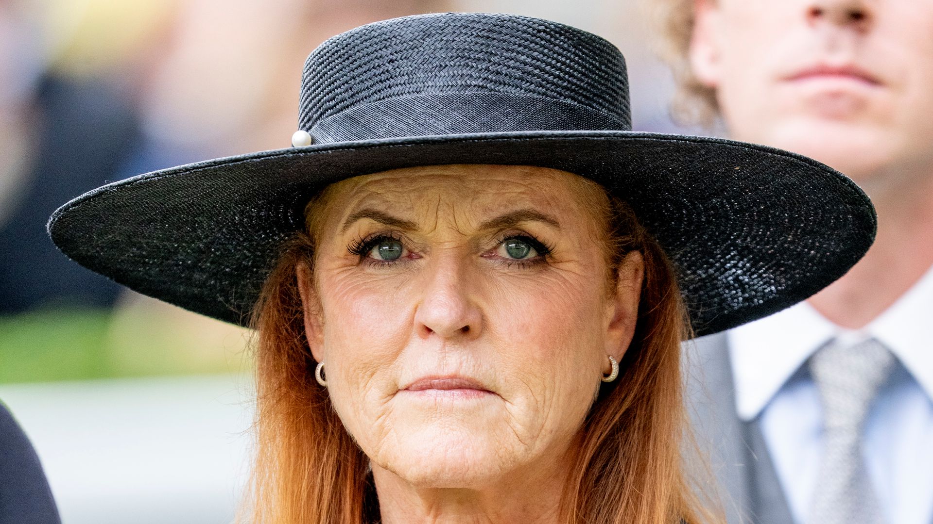 Sarah Ferguson attends a public event wearing a black hat and earrings, appearing thoughtful and composed.