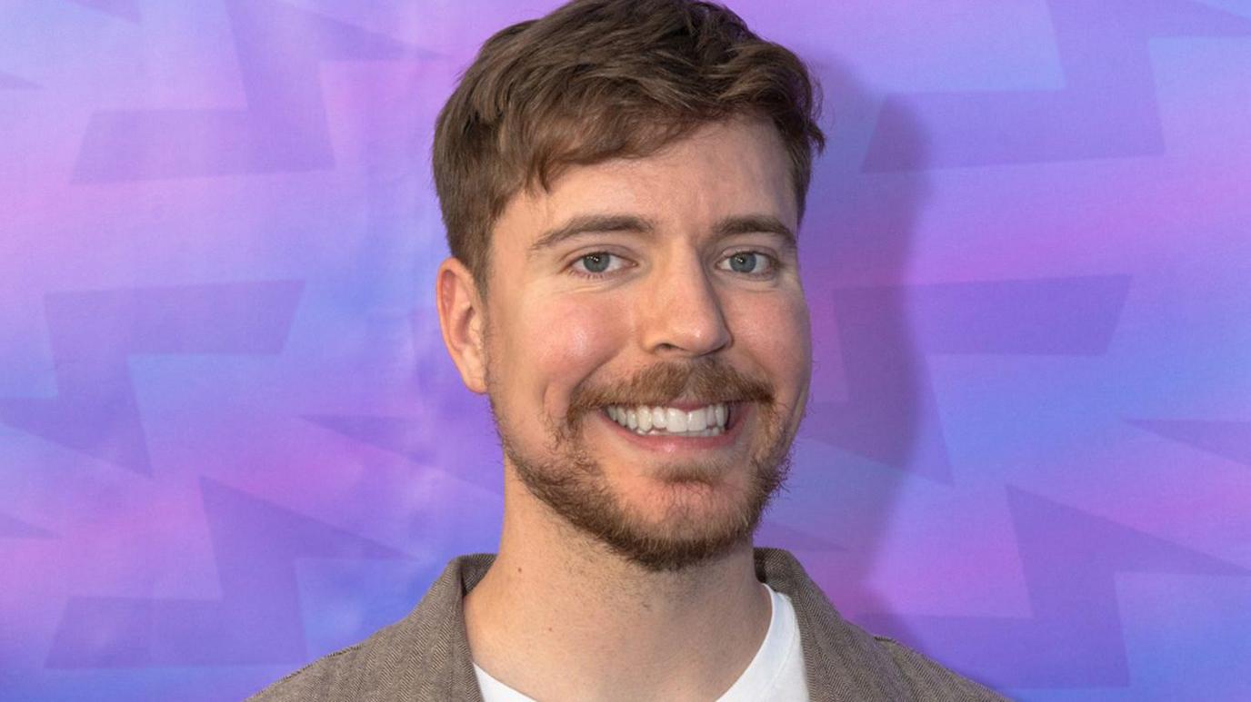 MrBeast, also known as Jimmy Donaldson, smiling at a media event against a purple background, following news of his company’s trademark filing for “MrBeast Financial” with crypto and fintech ambitions.