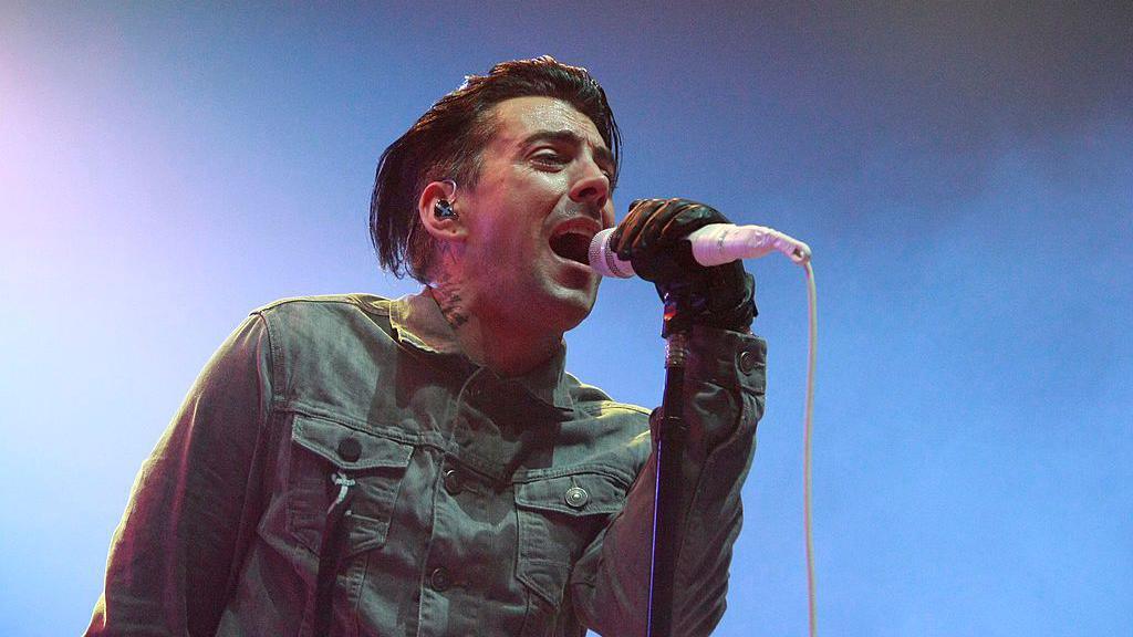 Ian Watkins singing passionately on stage as the lead vocalist of Lostprophets, performing in front of a cheering crowd.