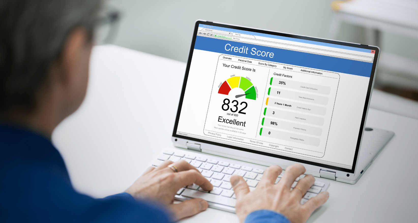 A man sitting at a desk checking his credit score on a laptop screen displaying a credit report dashboard.