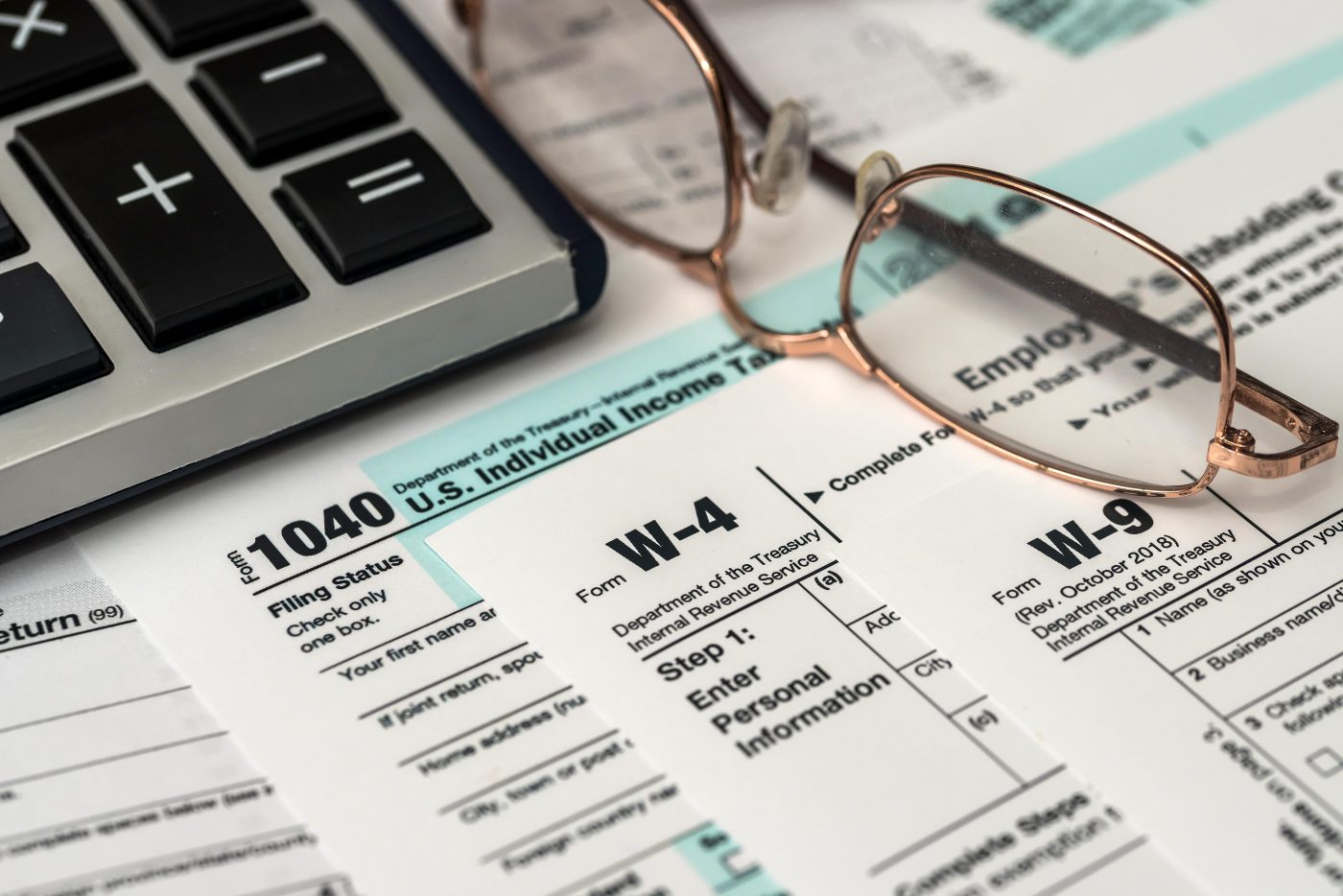 Tax documents laid out on a desk with glasses, a pen, and a calculator resting on top, representing financial review and tax preparation.