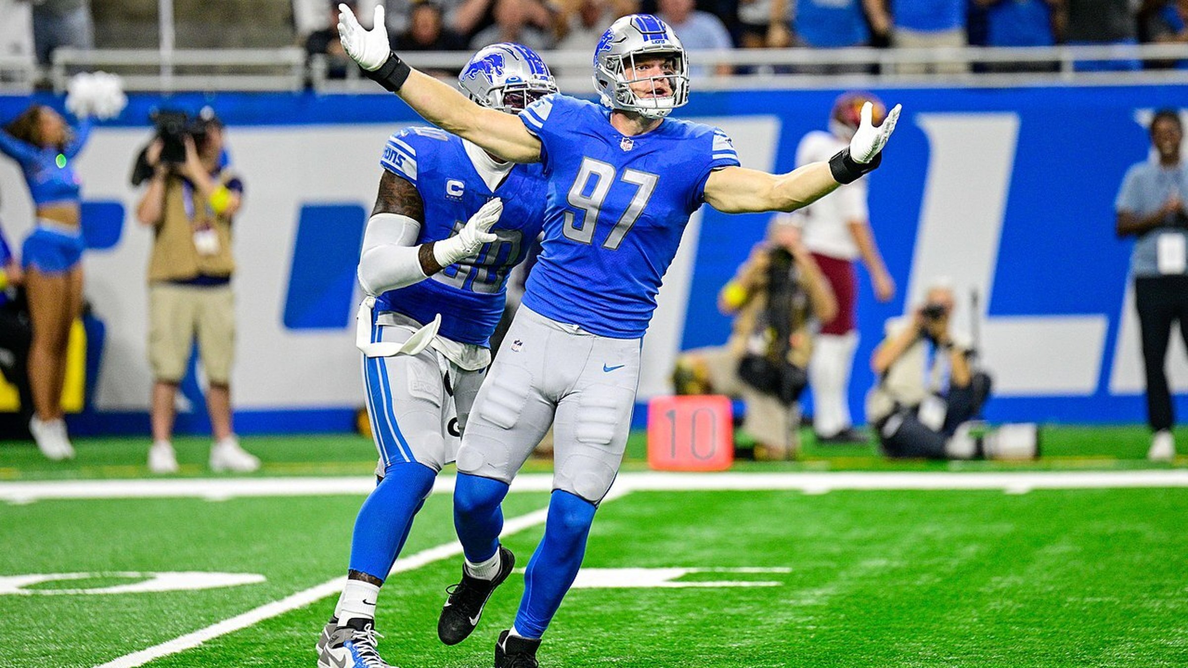 Aidan Hutchinson celebrates with arms wide open on the football field during a Detroit Lions game.
