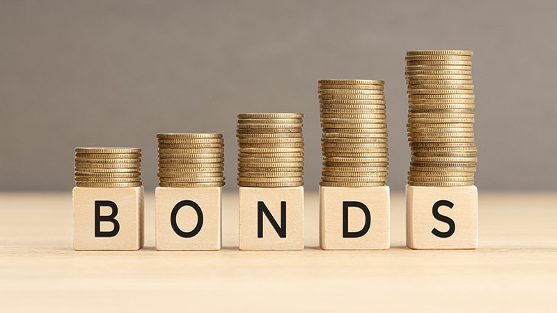 Wooden blocks spelling out "BONDS" with stacks of coins placed on top.