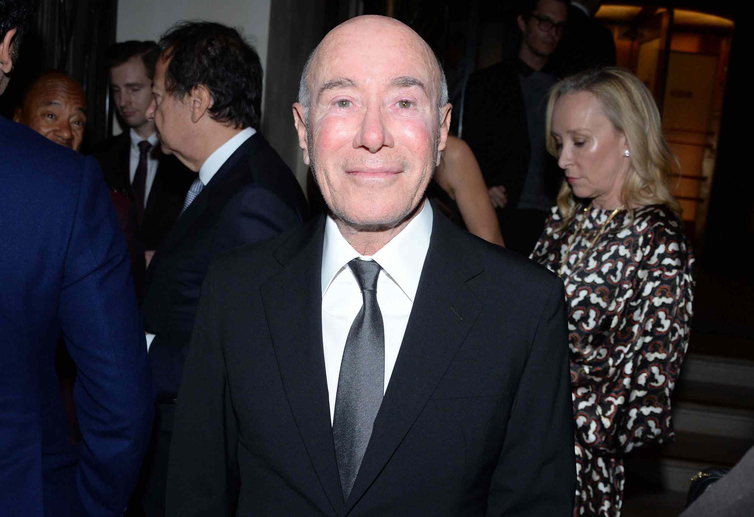 David Geffen wearing a tailored suit at a business event, speaking with other attendees.