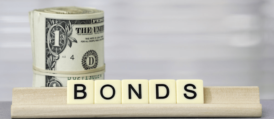 Scrabble letters spelling out the word "BONDS" placed in front of a wad of cash.