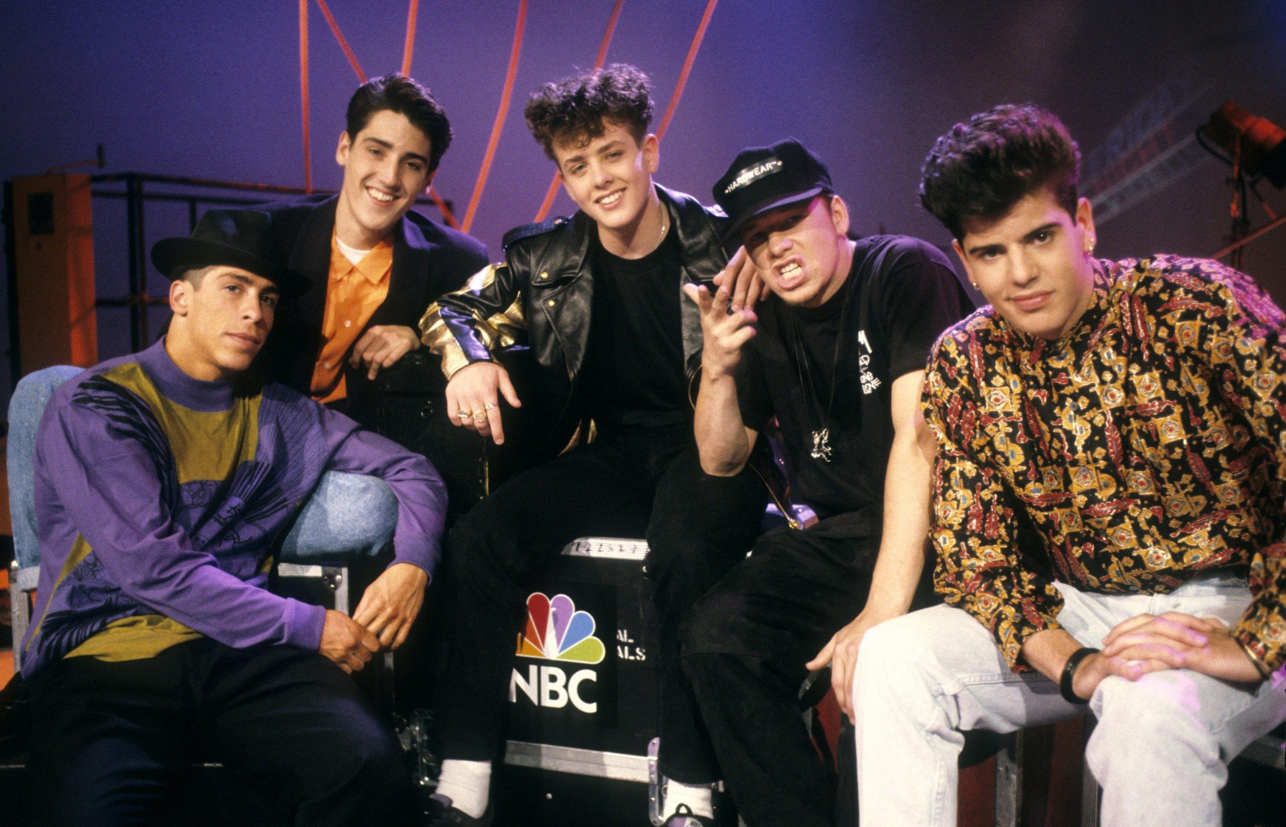 New Kids on the Block posing backstage at an NBC studio in the late 1980s, wearing colorful outfits during their rise to pop superstardom.