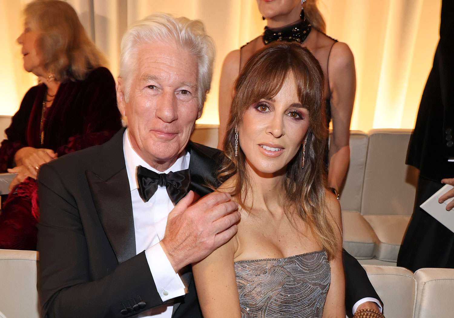 Richard Gere seated next to his wife Alejandra Silva at a gala dinner, both dressed elegantly.