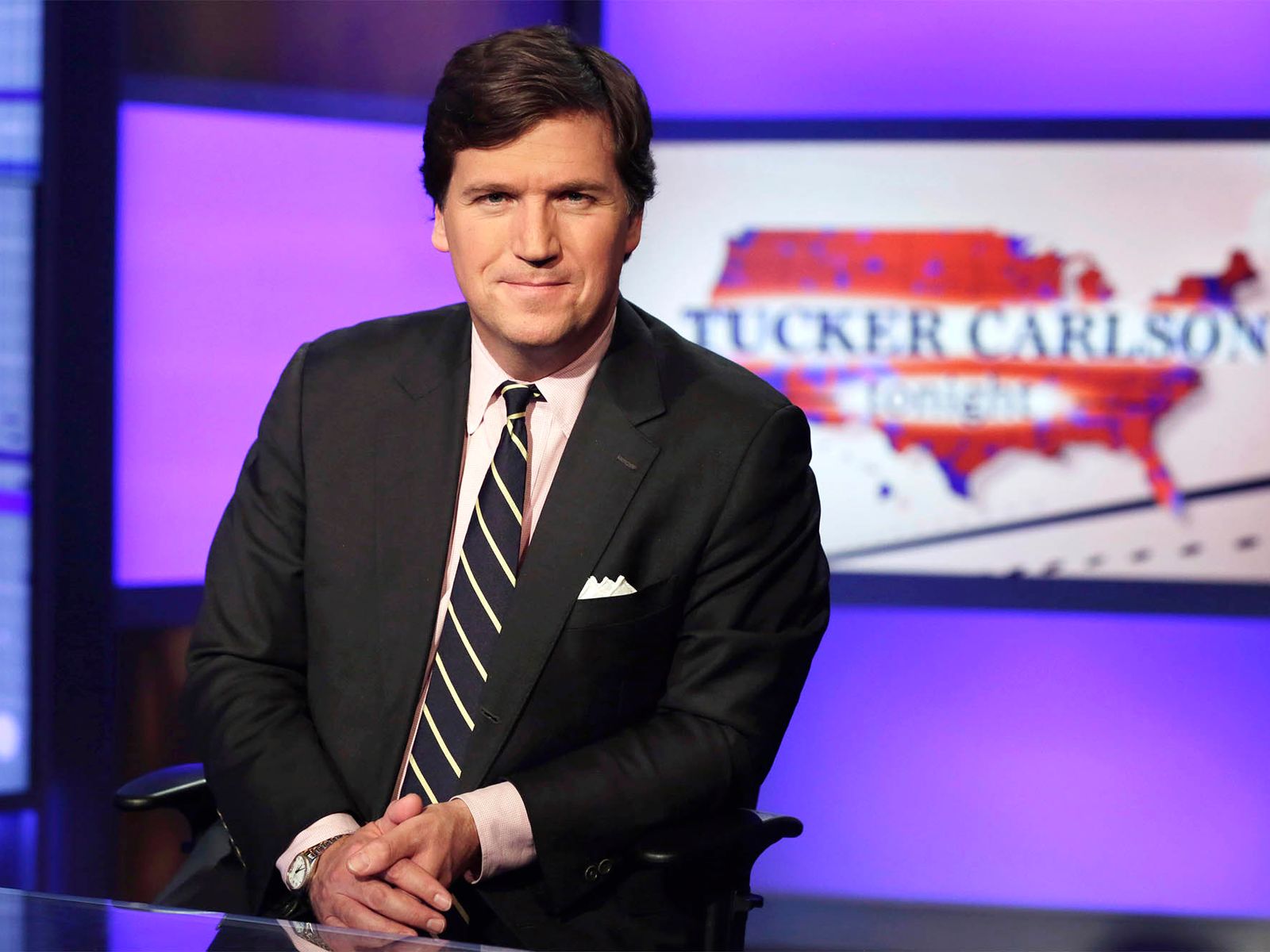 Tucker Carlson presenting his show on set, speaking to the camera.