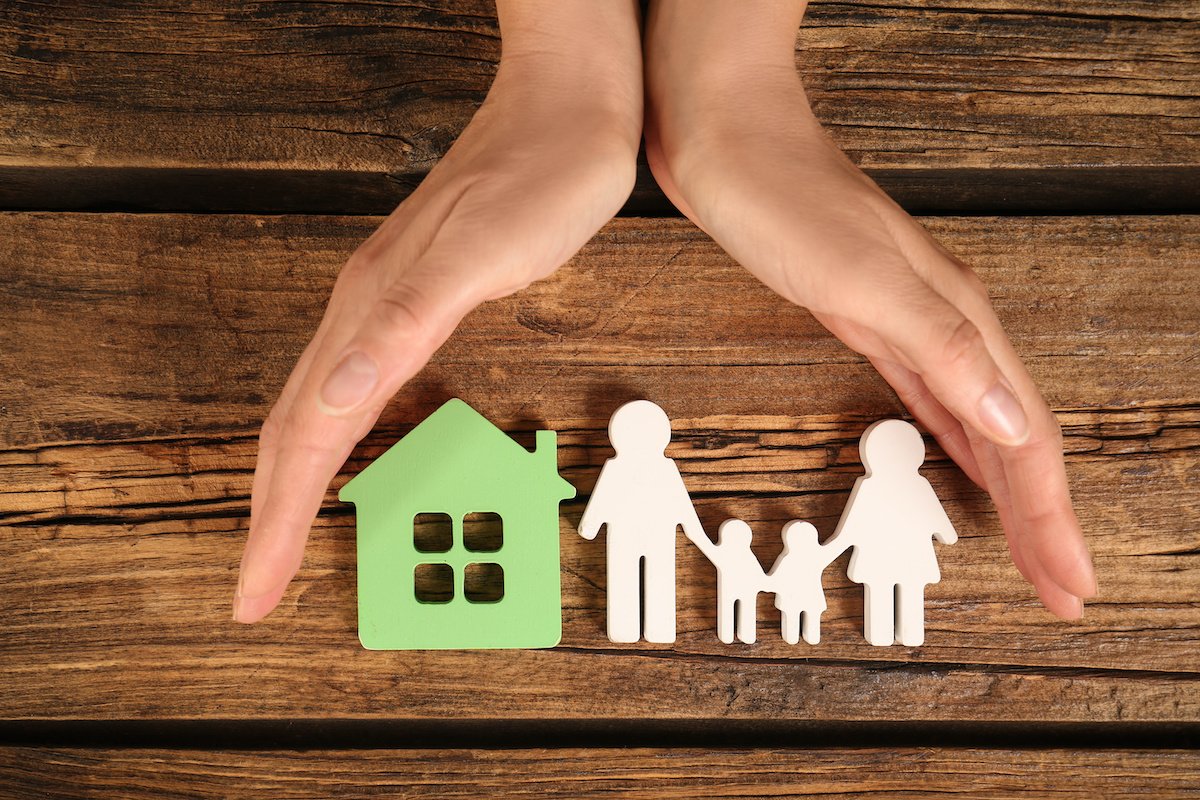 Two hands gently shielding a paper cutout of a family and a house, symbolizing estate planning and financial protection.
