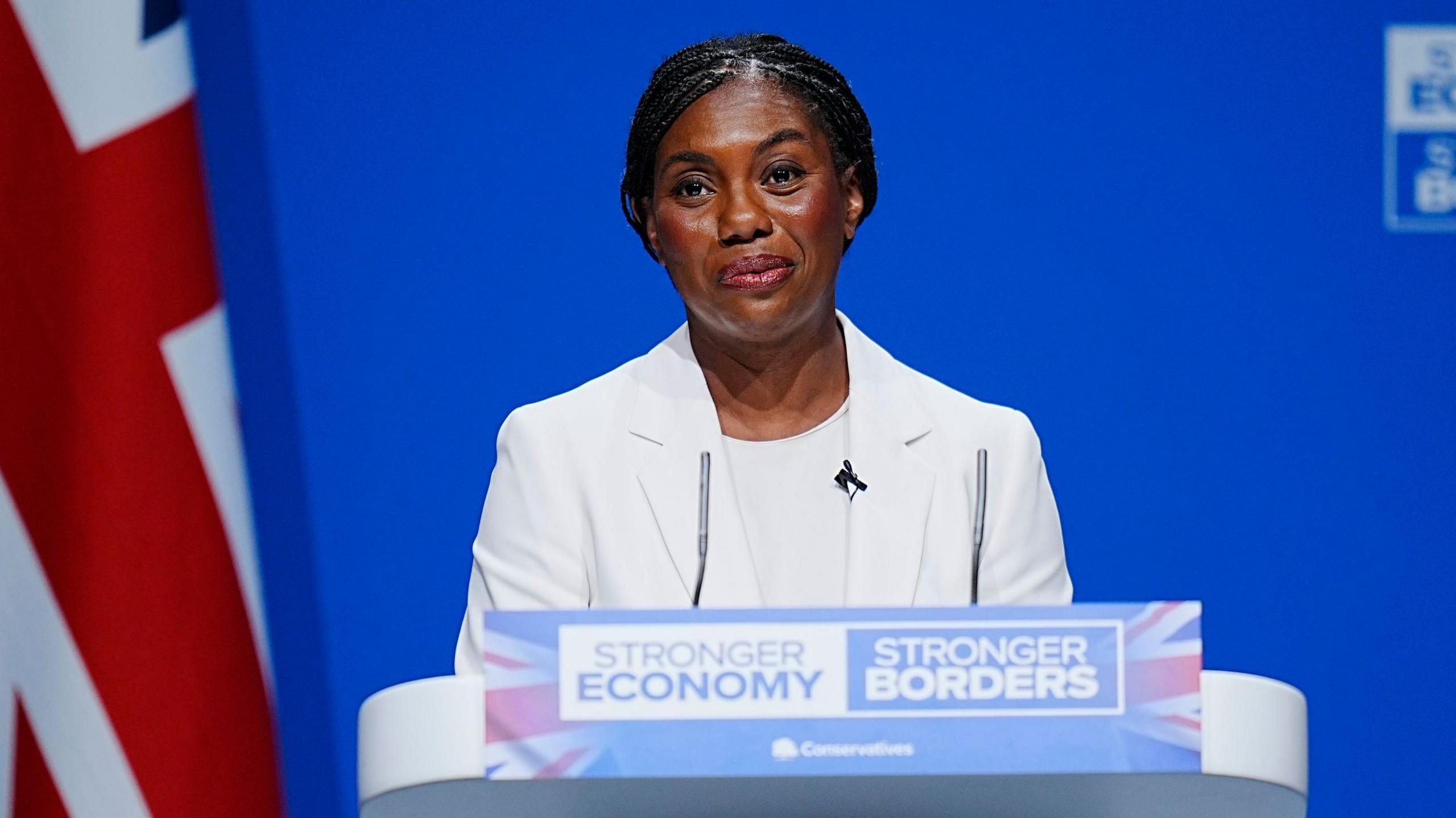 Kemi Badenoch delivering a speech at the Conservative Party Conference, standing at the podium with the party logo behind her.