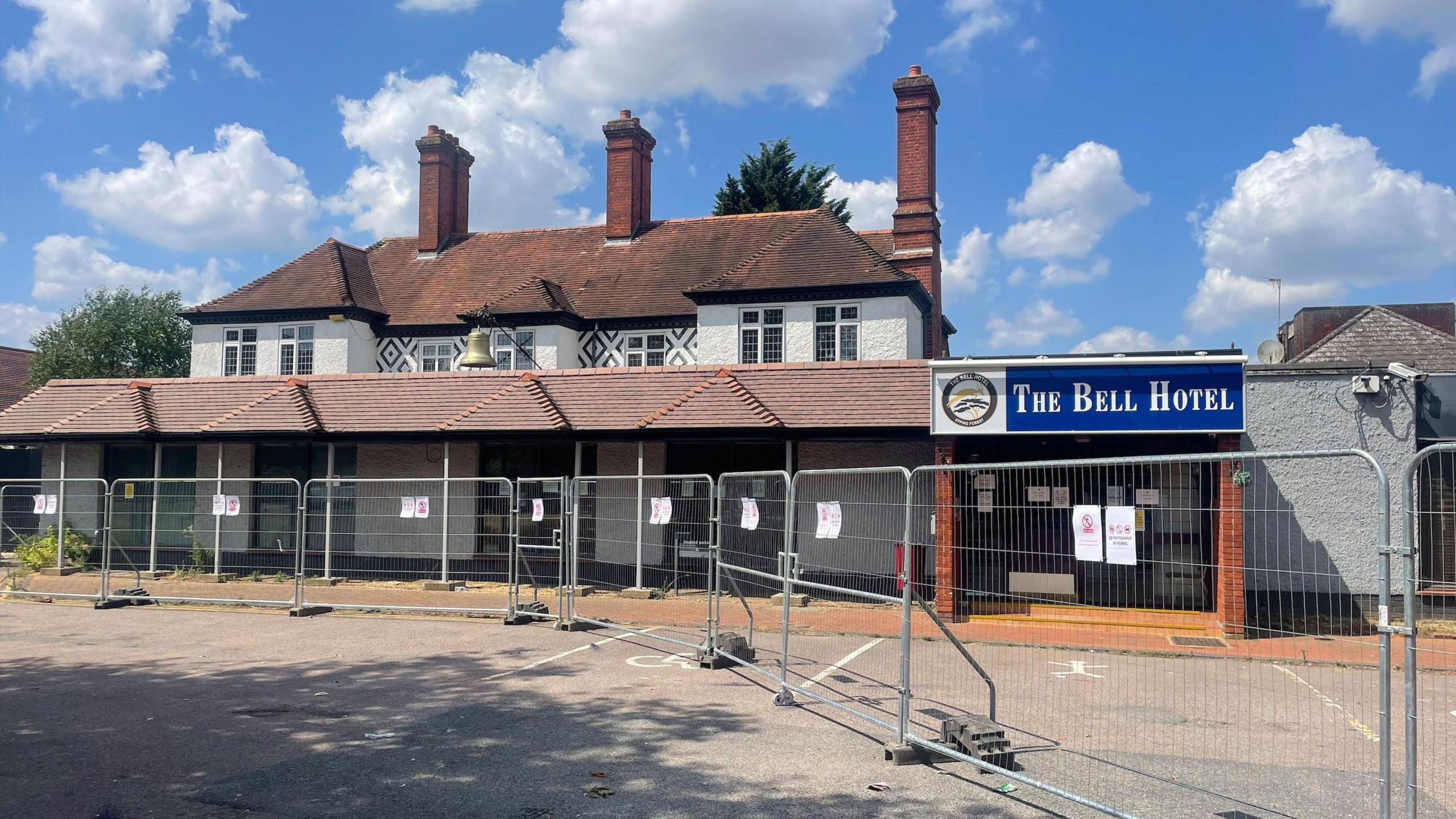 A boarded-up and fenced-off former asylum hotel with signs warning the public, while some former residents refuse to leave the premises.