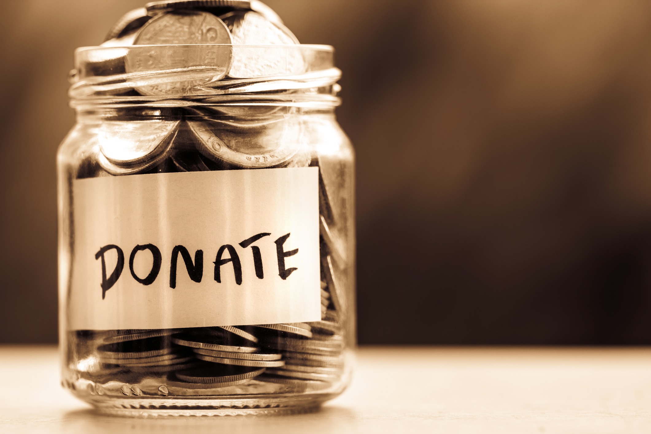 Clear donation jar filled with coins representing charitable giving and savings