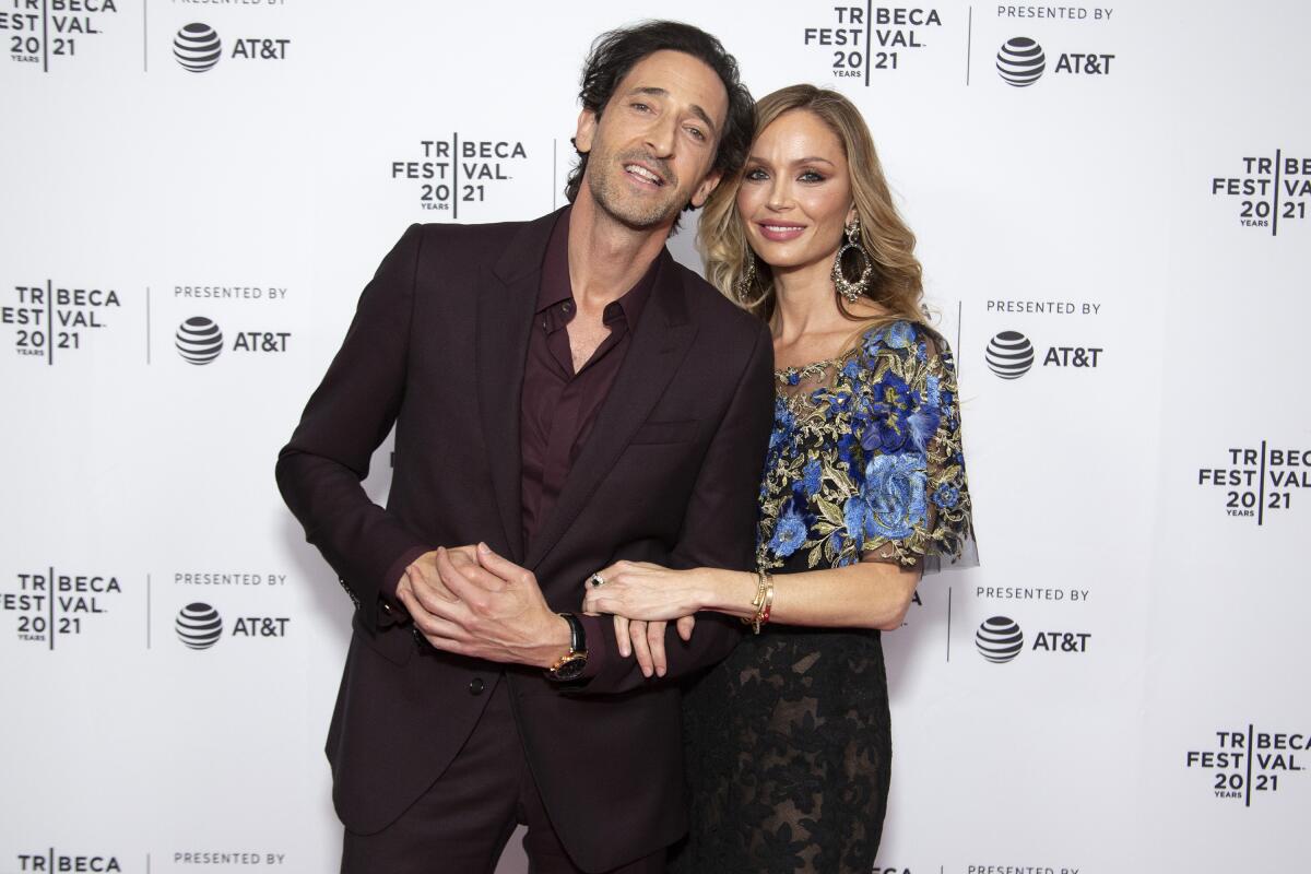 Georgina Chapman and Adrien Brody walk the red carpet together, smiling and posing for photographers at a high-profile event.