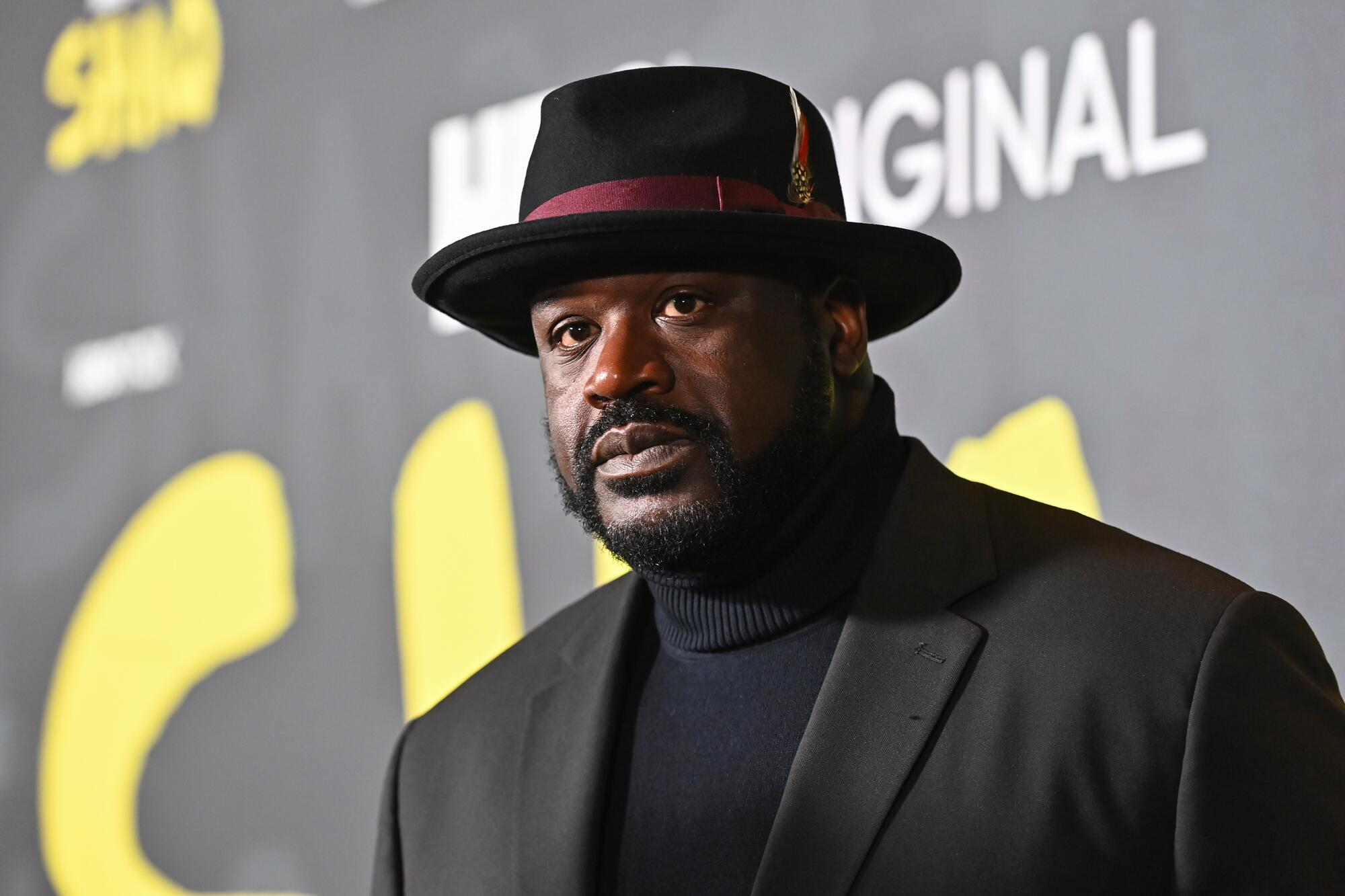 Shaquille O’Neal wearing a stylish hat and suit while posing on the red carpet.