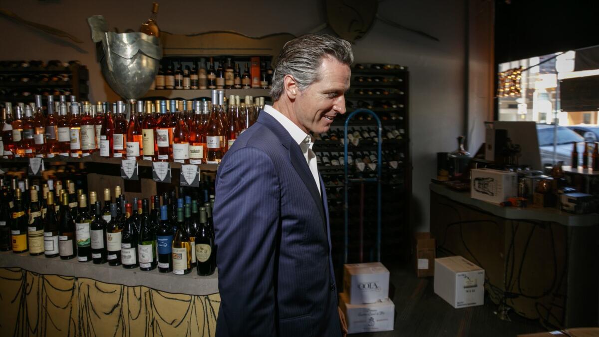 Gavin Newsom inside his winery surrounded by shelves filled with hundreds of wine bottles.