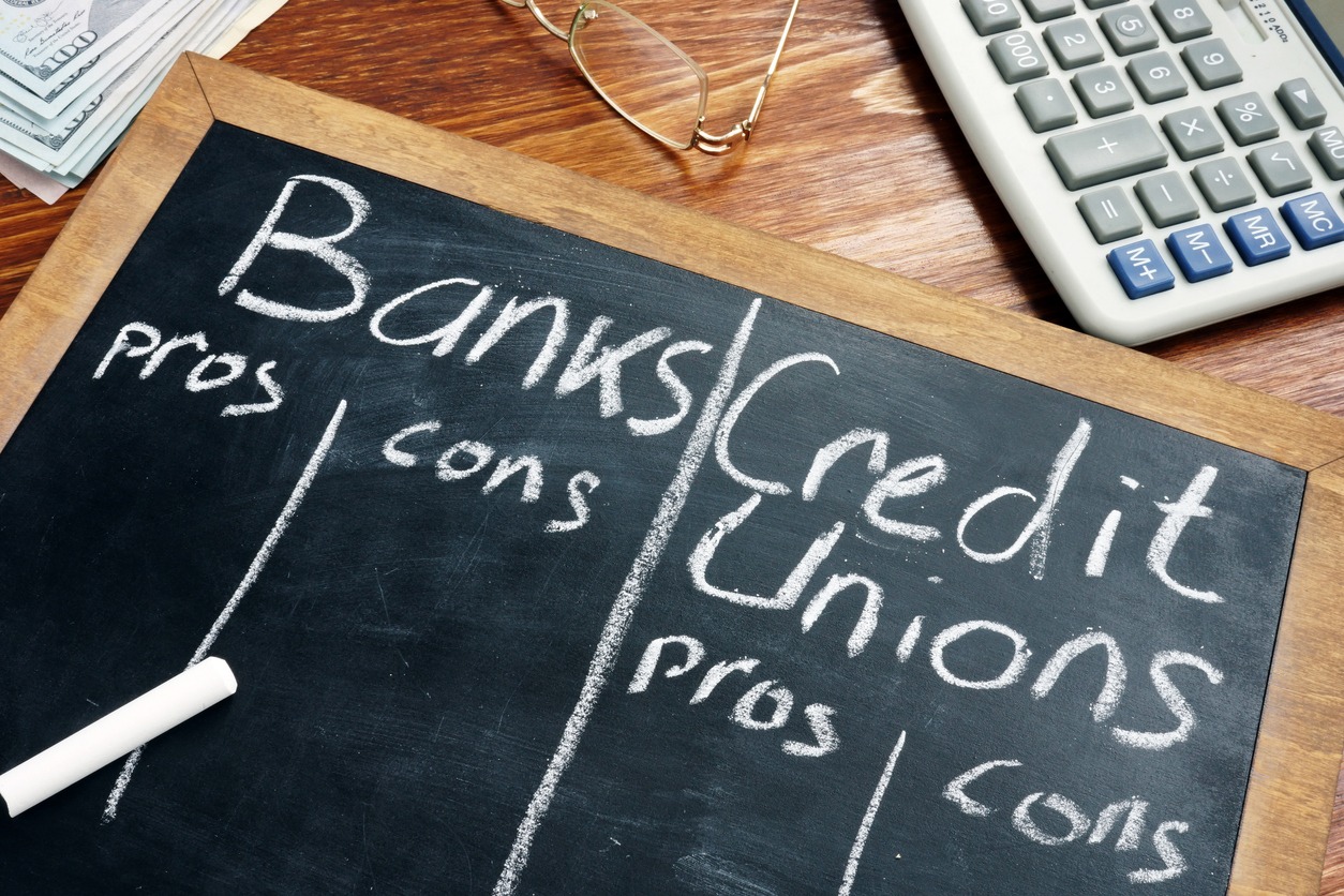 banks vs. credit unions pros and cons written on a blackboard.