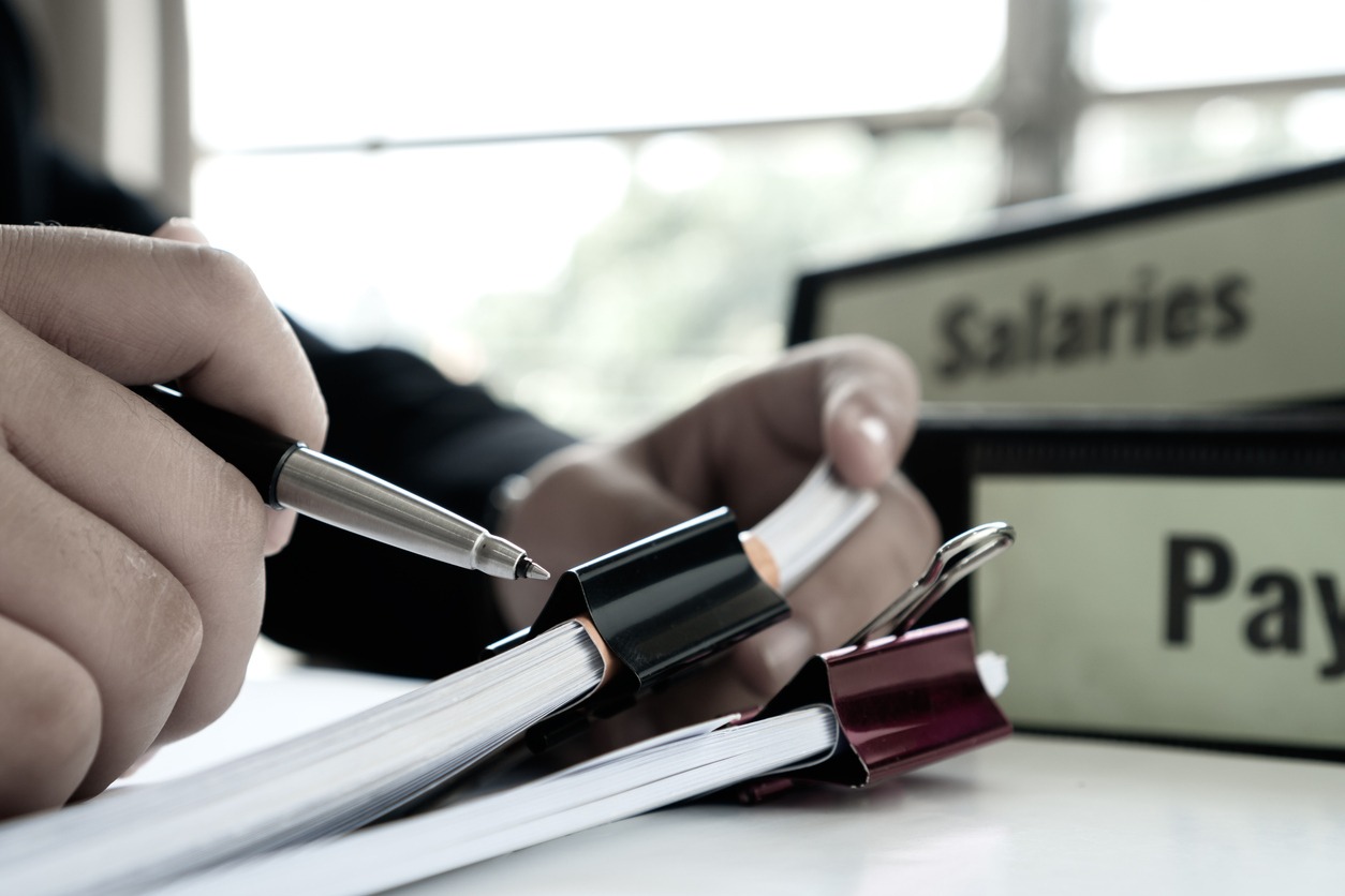 document report or business management concept: businessman manager hands holding pen for reading, signing paperwork near payroll salary binder, summary report hr human resources business bookkeeping