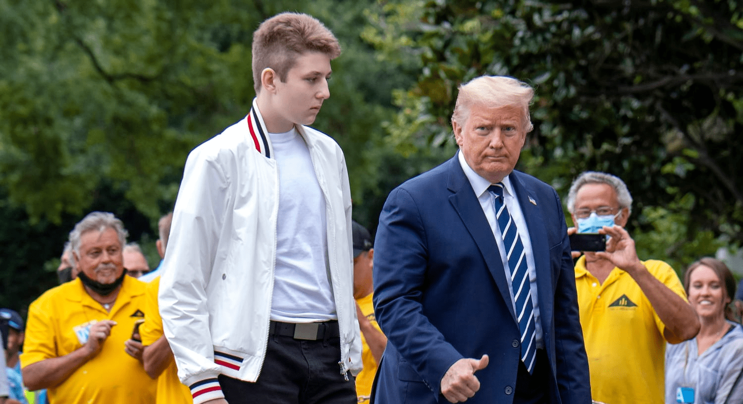 Donald Trump walks alongside his son Barron Trump outdoors, with onlookers in the background, during a public appearance.
