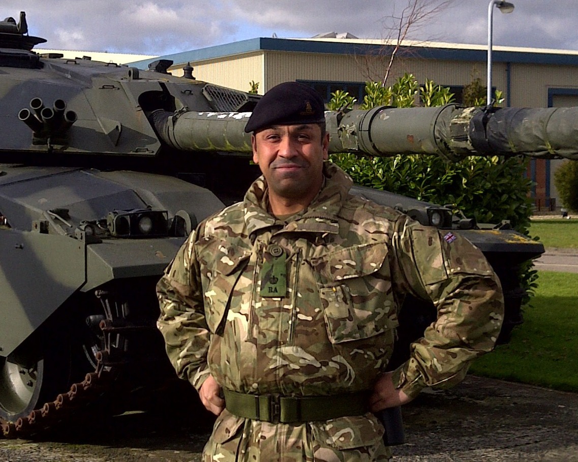James Cleverly in army uniform standing in front of a military tank