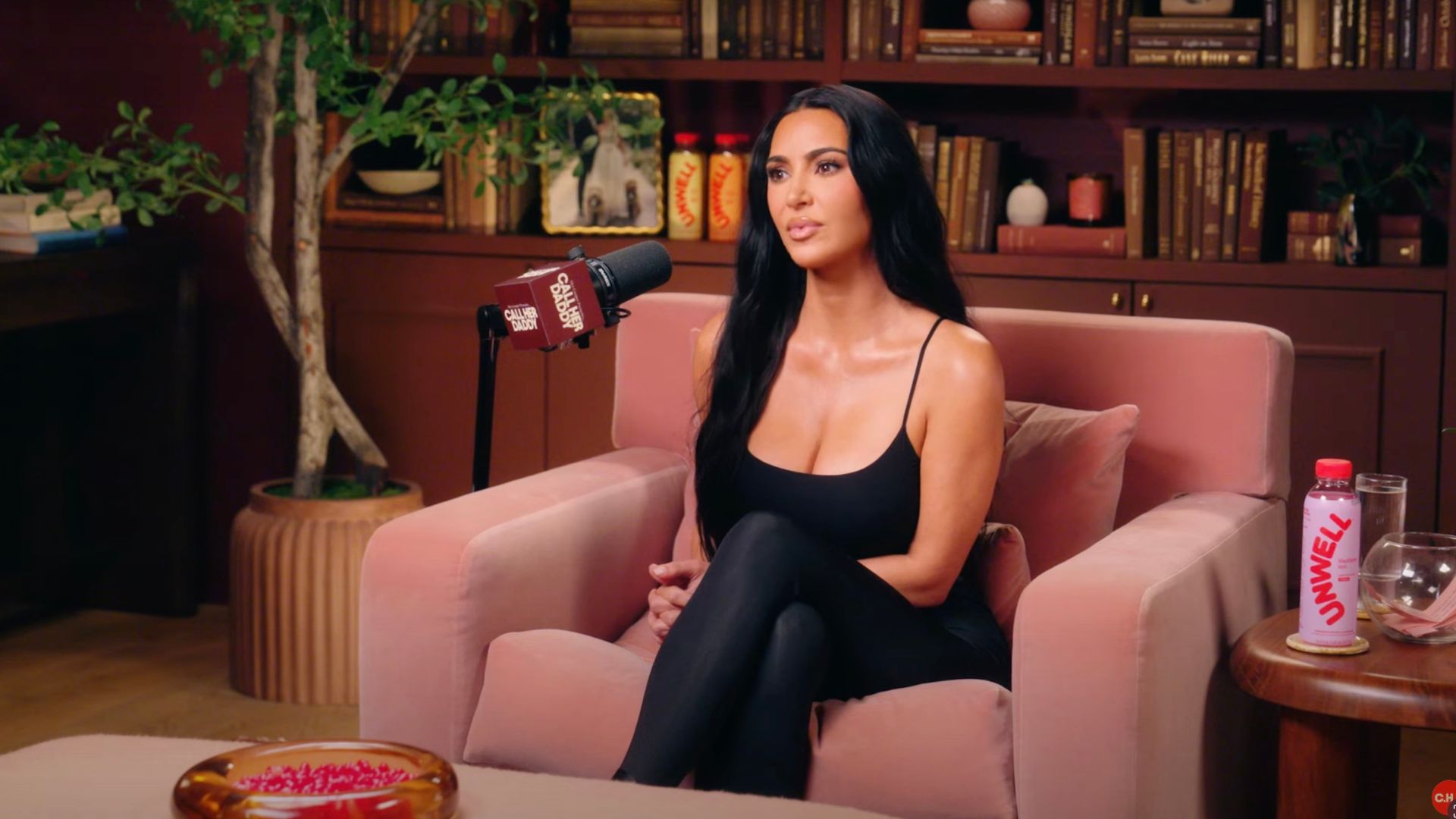 Kim Kardashian sits across from Alex Cooper in the Call Her Daddy studio, engaged in a candid conversation surrounded by soft studio lighting and microphones.