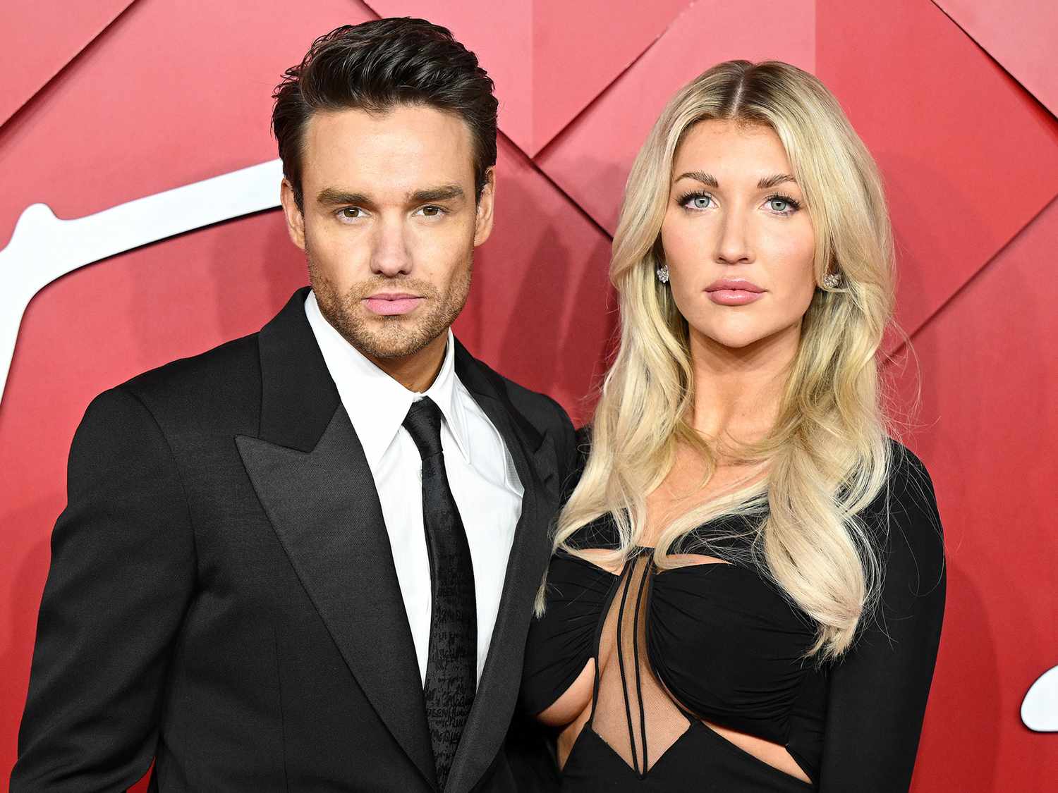 Kate Cassidy in a black ball gown and Liam Payne in a black suit posing together on the red carpet at an awards show.