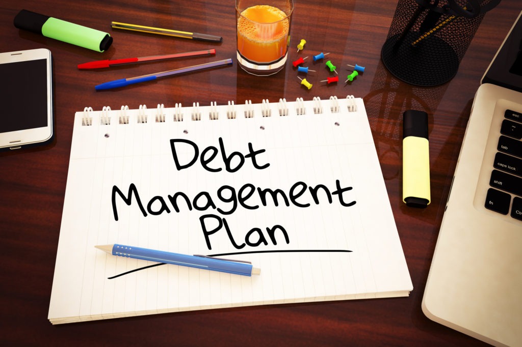 A notepad on a table showing a debt management plan, surrounded by a laptop and pens, ready for financial planning.
