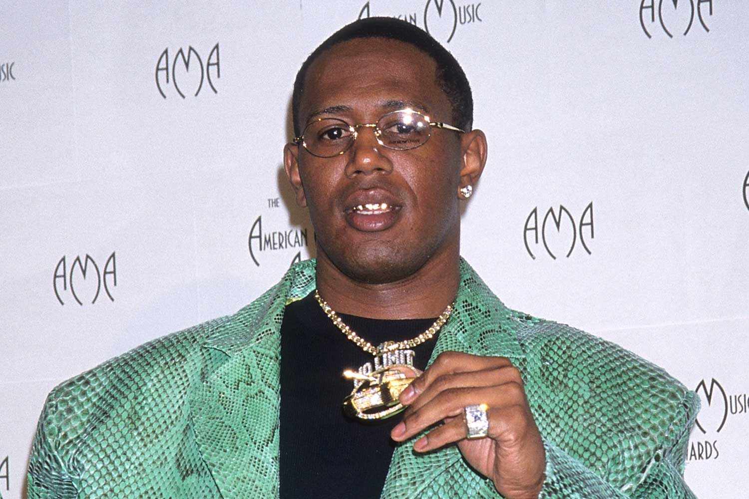 Master P showing off his diamond chains and rings on the red carpet, wearing a black suit and sunglasses.