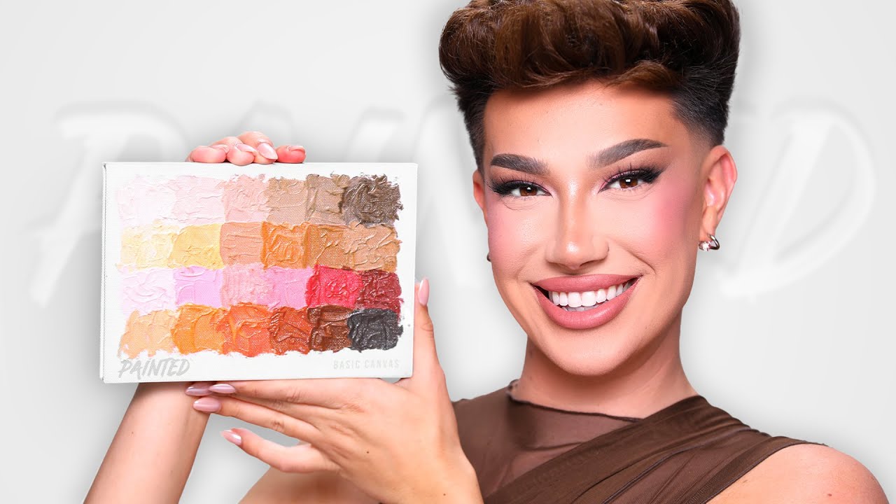 James Charles holding the latest Painted Artistry Canvas palette, showcasing its vibrant rainbow shades with a bright, proud smile.