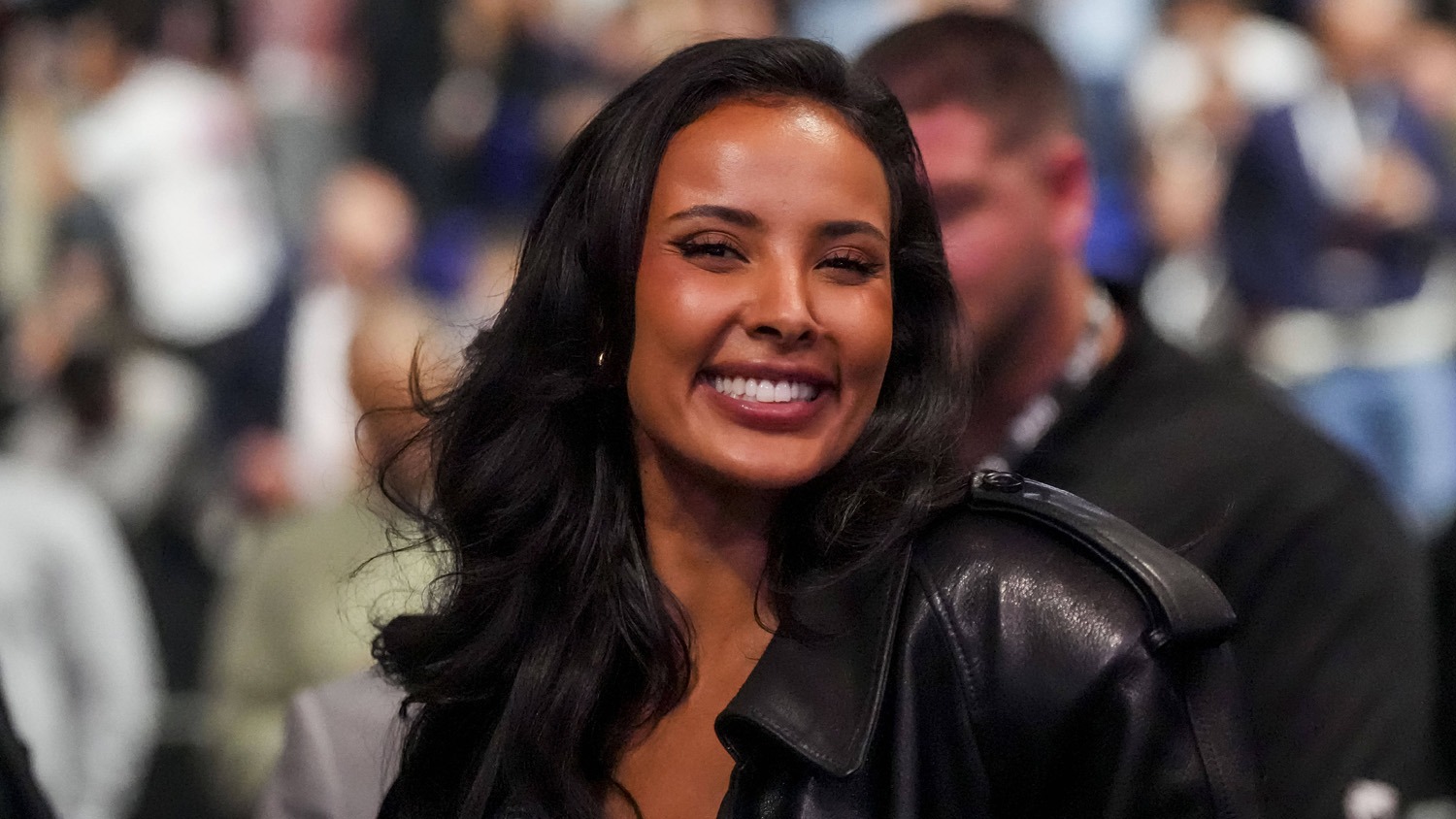 Maya Jama smiling and waving to the crowd at UFC London, radiating excitement and charisma.