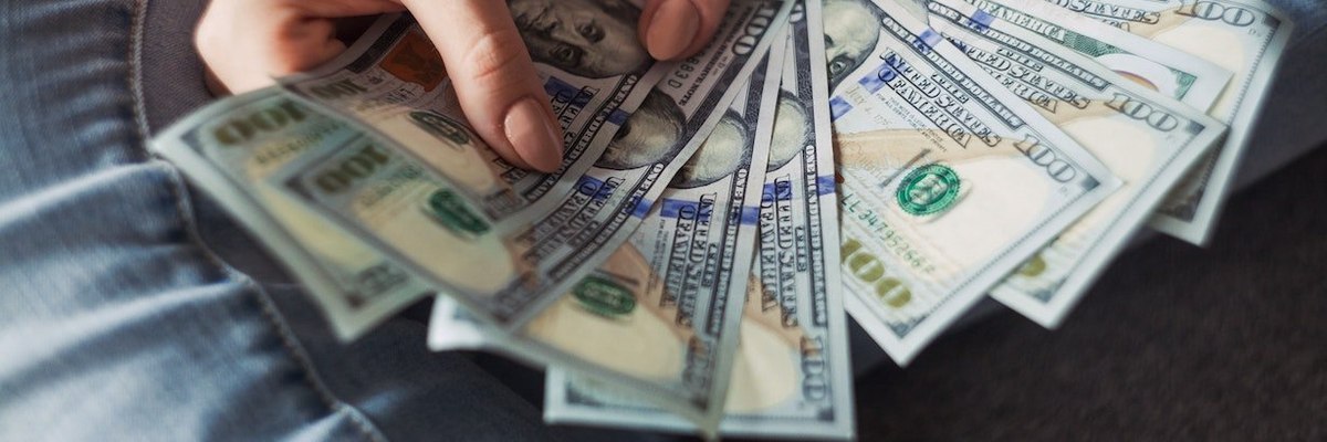 A hand counting a large stack of cash on a table.